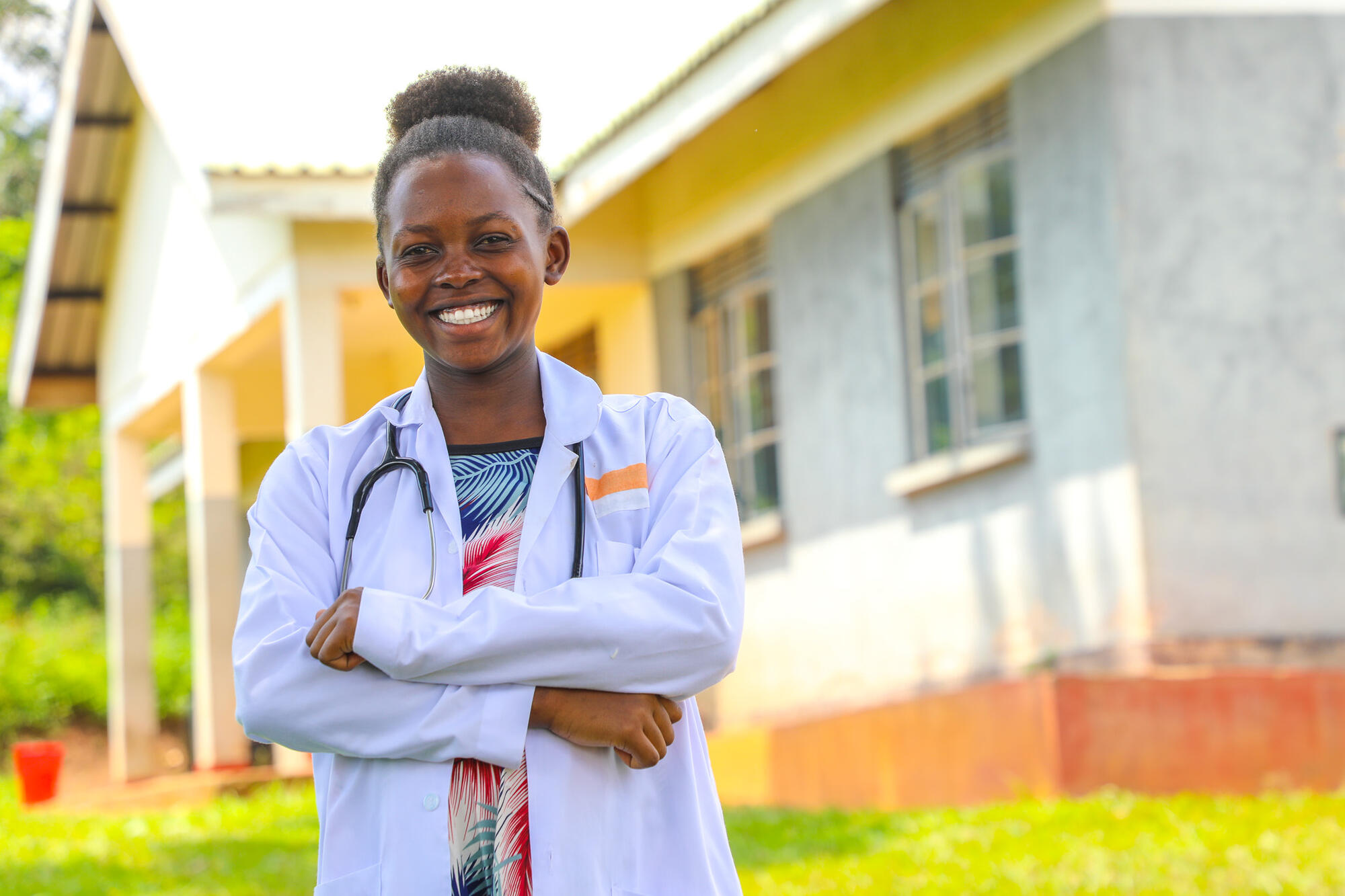 A women in a white coat and stethoscope stands similing at the camera. 