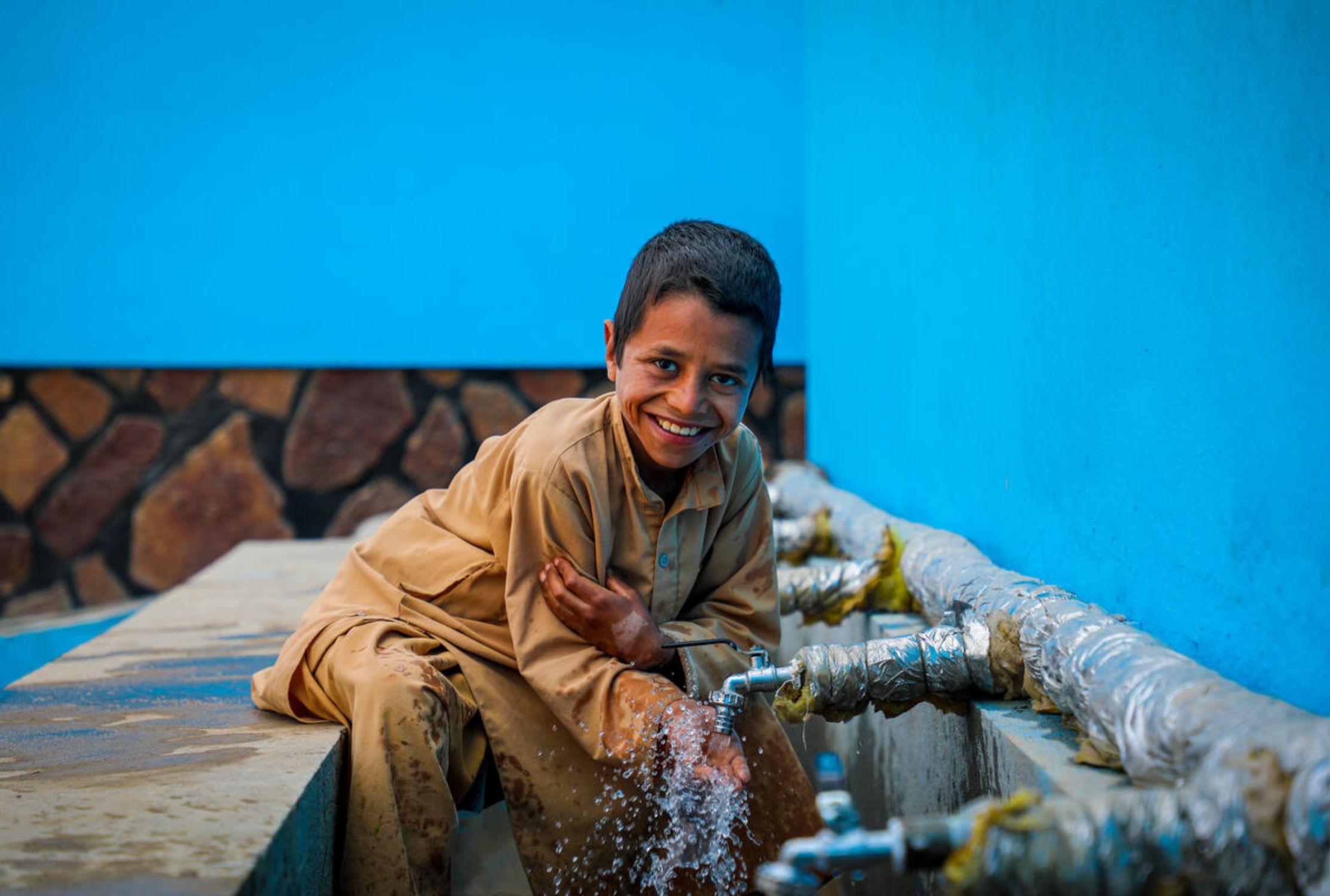 Afghan boy smiling next to a tap dispensing clean water