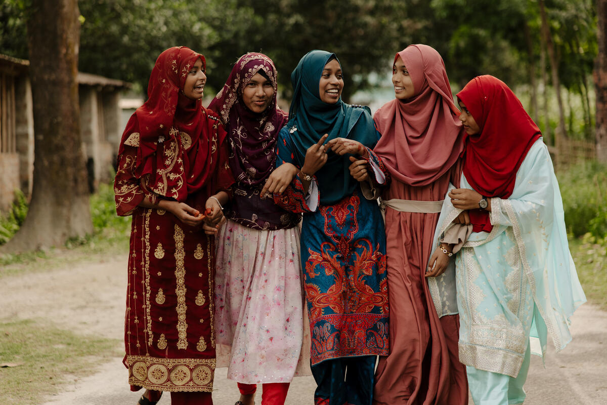 Misu walks with four other girls along a village road in Bangladesh, chatting together. 