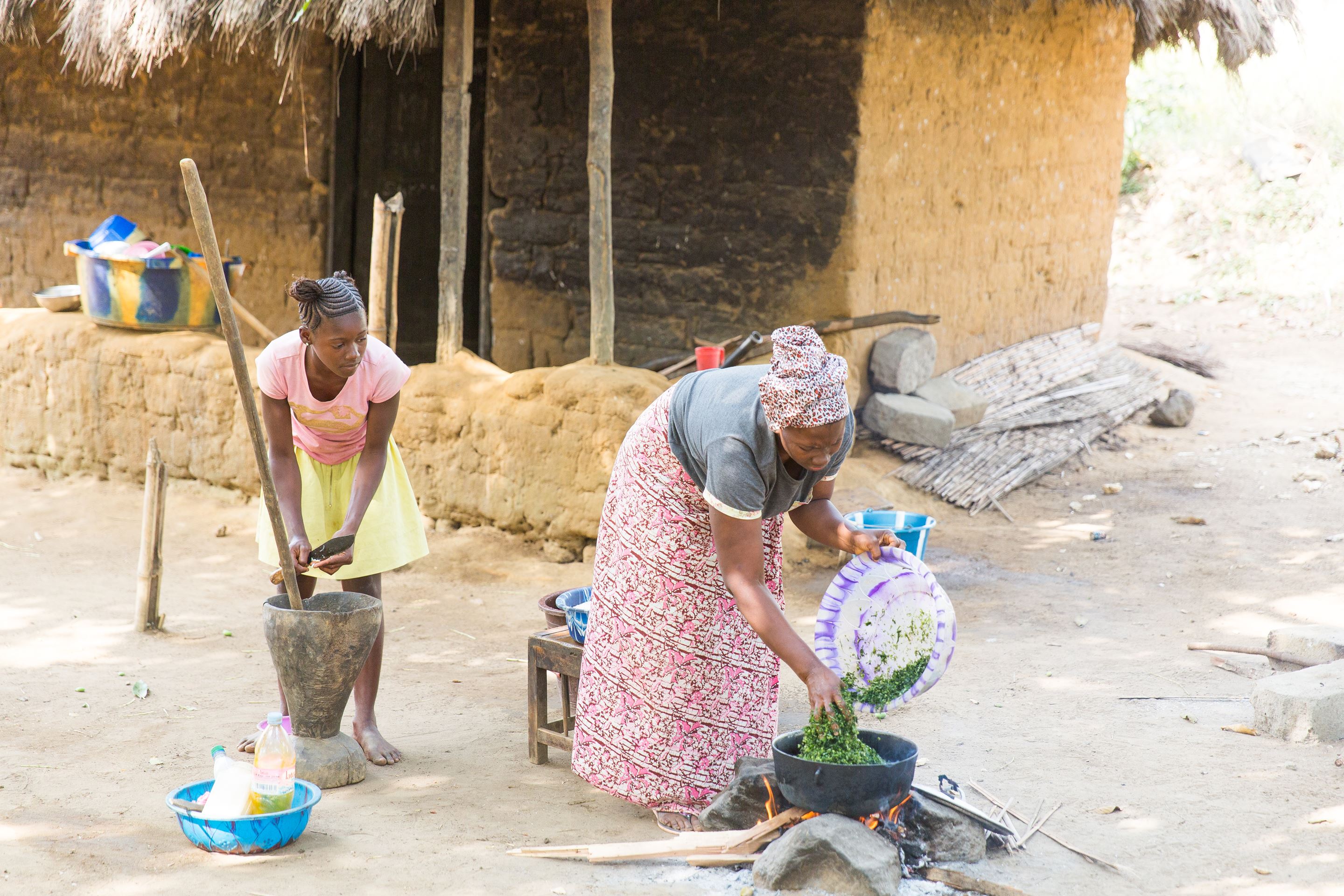 Woman and girl from Sierra Leone stand outside tending to the food they are cooking