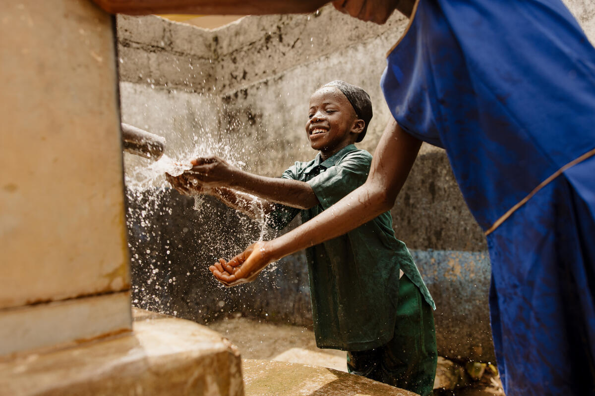Smiling school girl as she stands catching water at a tap, Sierra Leone.
