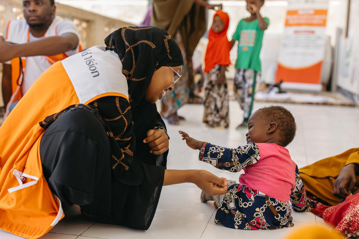 Baby girl playing with a female WV health member of staff, sat on the floor of a health clinic.