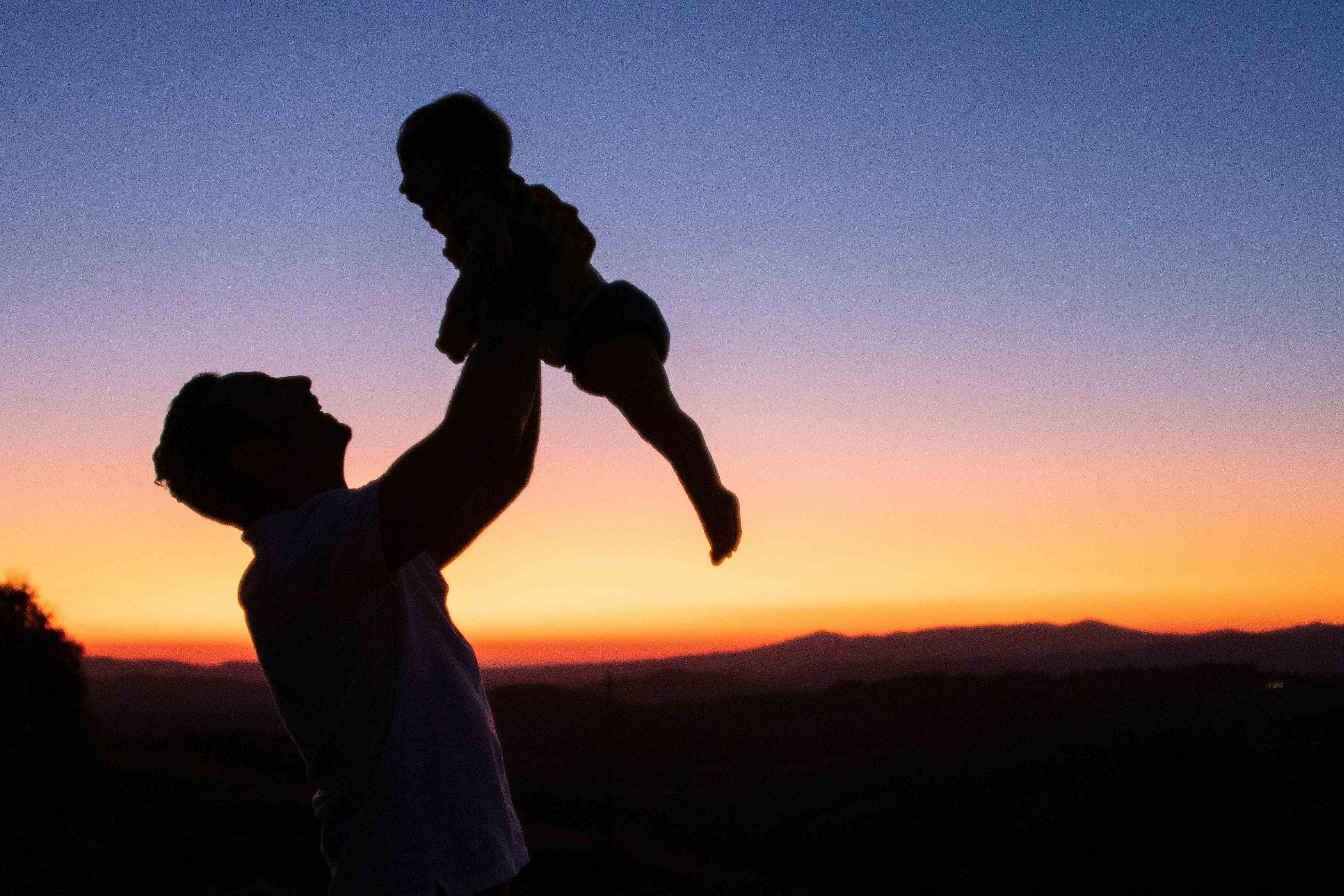 Silhouette of a father lifting young child. The background shows a sunset
