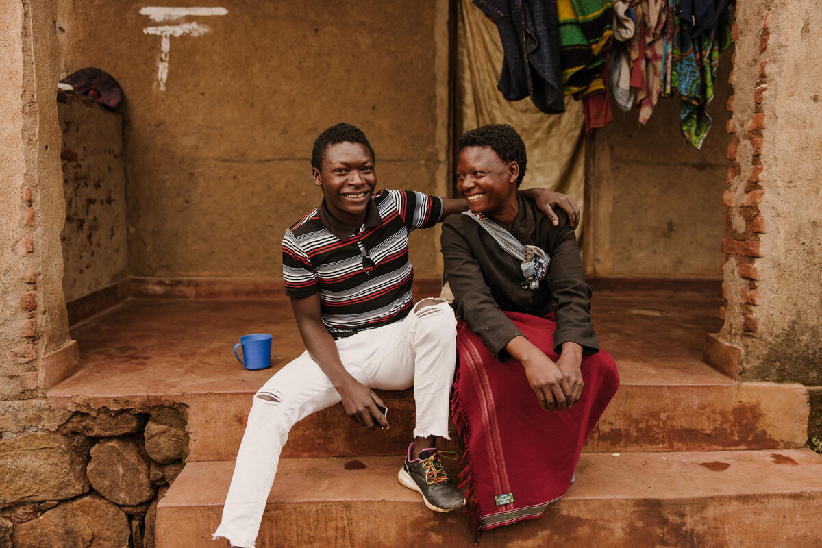 Moses, a former sponsored child in Malawi, the first in his family to go to university sits with his mother on the steps at the front of their house