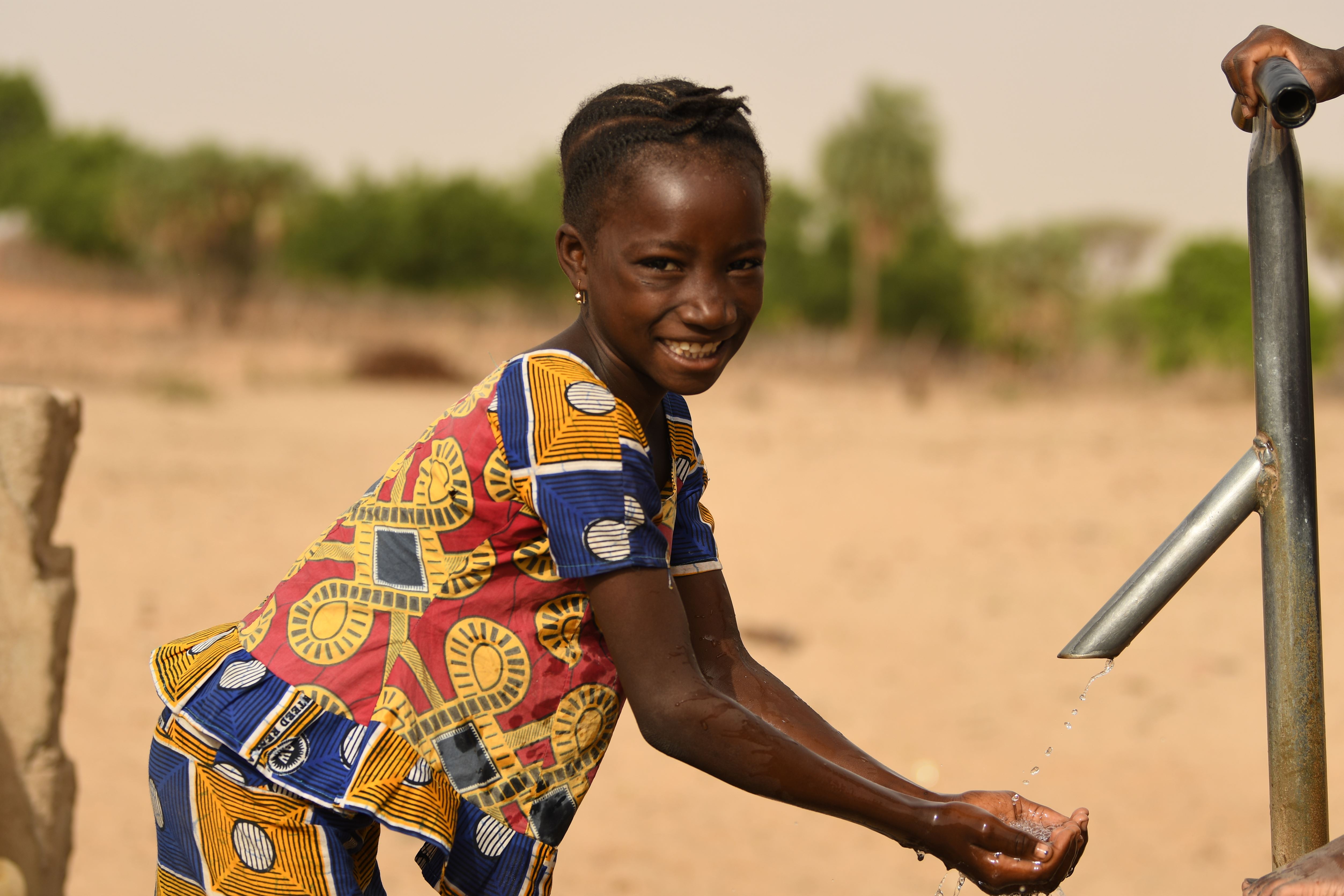 Sponsored child in Niger smiles as she washes her hands from a clean water tap