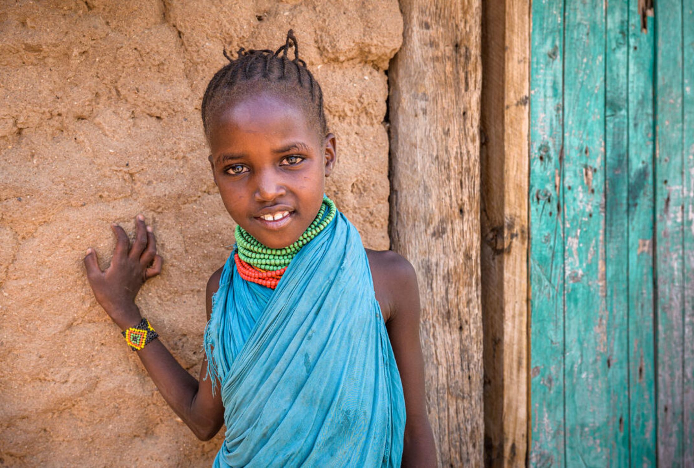 Seven-year-old Kenyan girl stands outside her home smiling