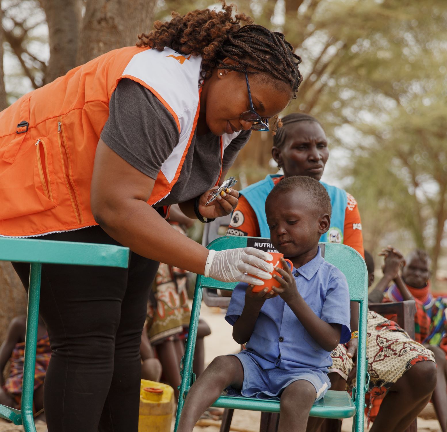 World Vision staff member helping feed Kenyan boy