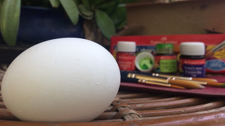 Image of a boiled egg, with paints, brushes and other craft materials in the background