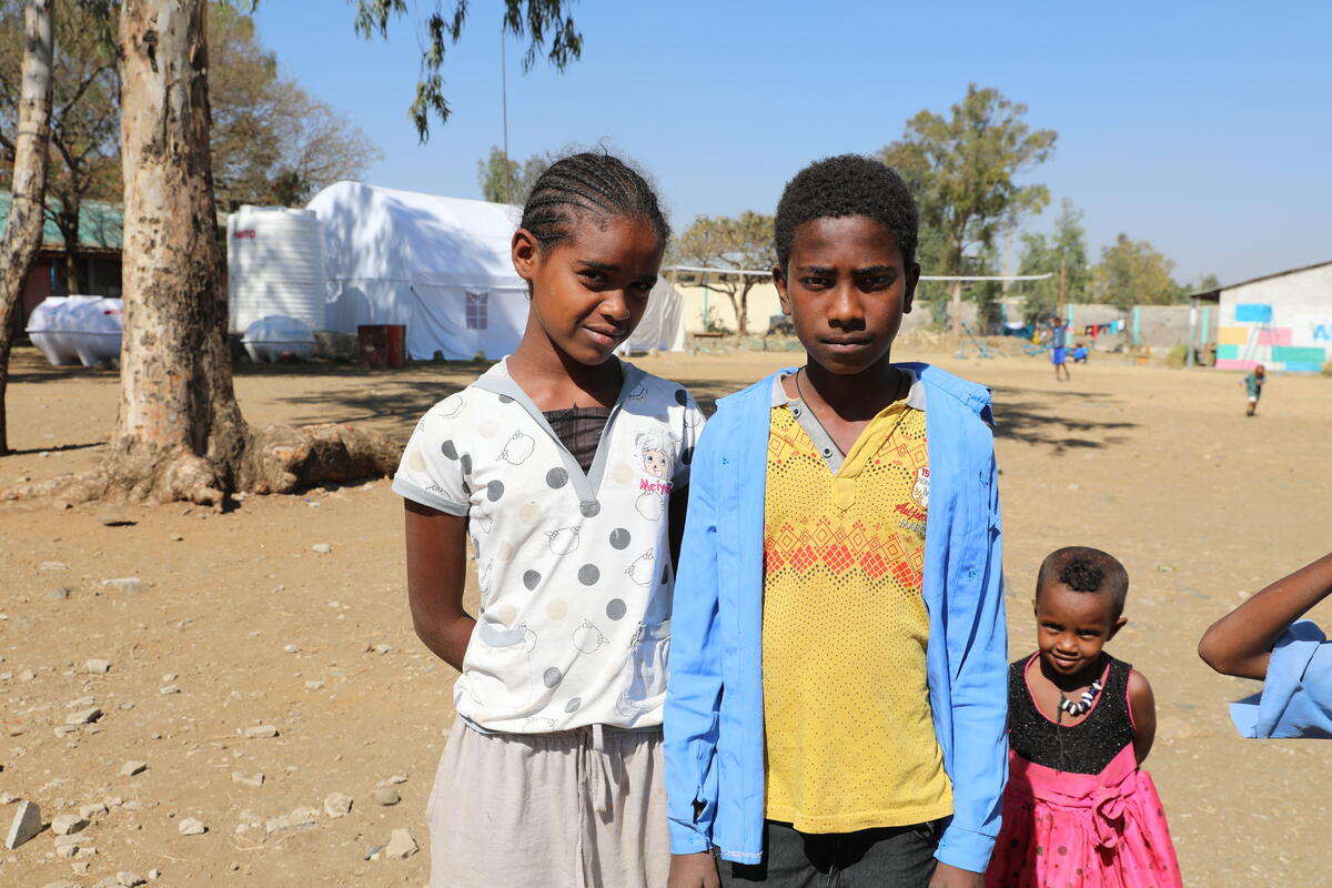 A group of three children including 12-year-orald Yonas, stand in a makeshift refugee camp in northern Ethiopia, looking at the camera.