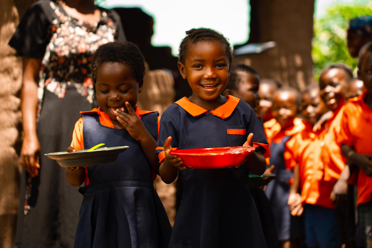 Two young girls in school uniform, holding plates of food provided by World Vision, Malawi