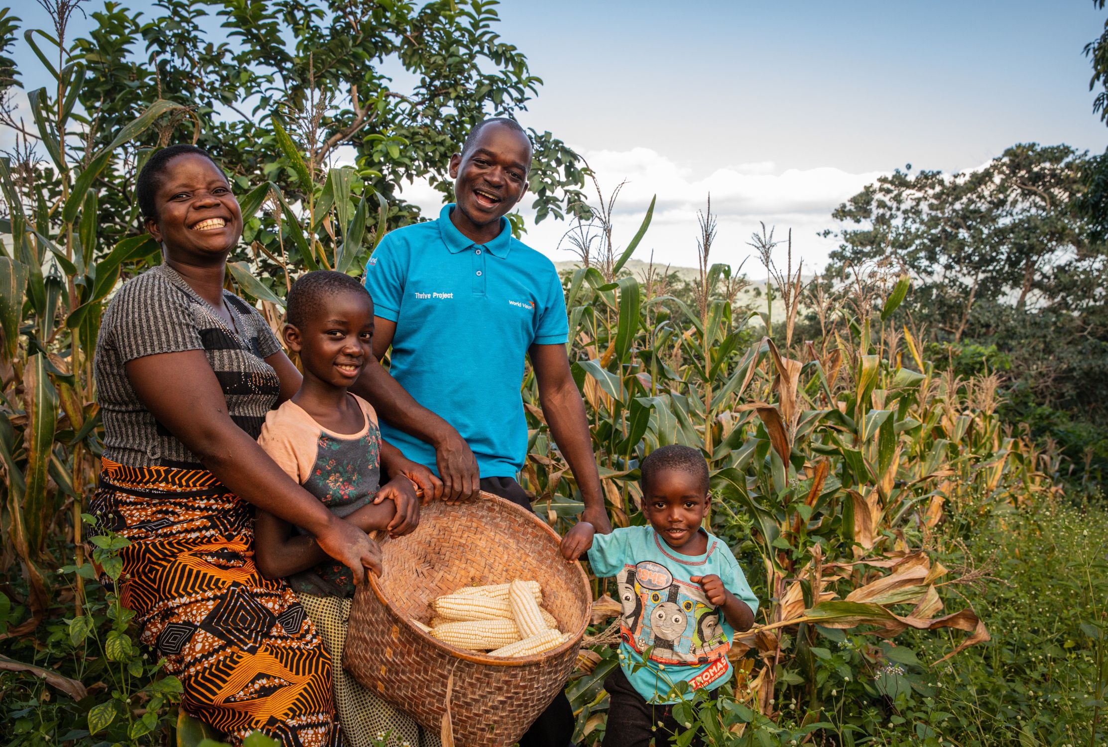 Family from Malawi smiling and holding a basket filled with corn