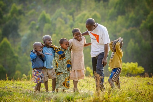 World Vision staff member with five children stood in a green field looking at each other