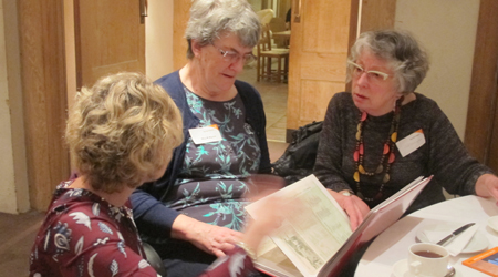 Three people sit around a table and read a paper