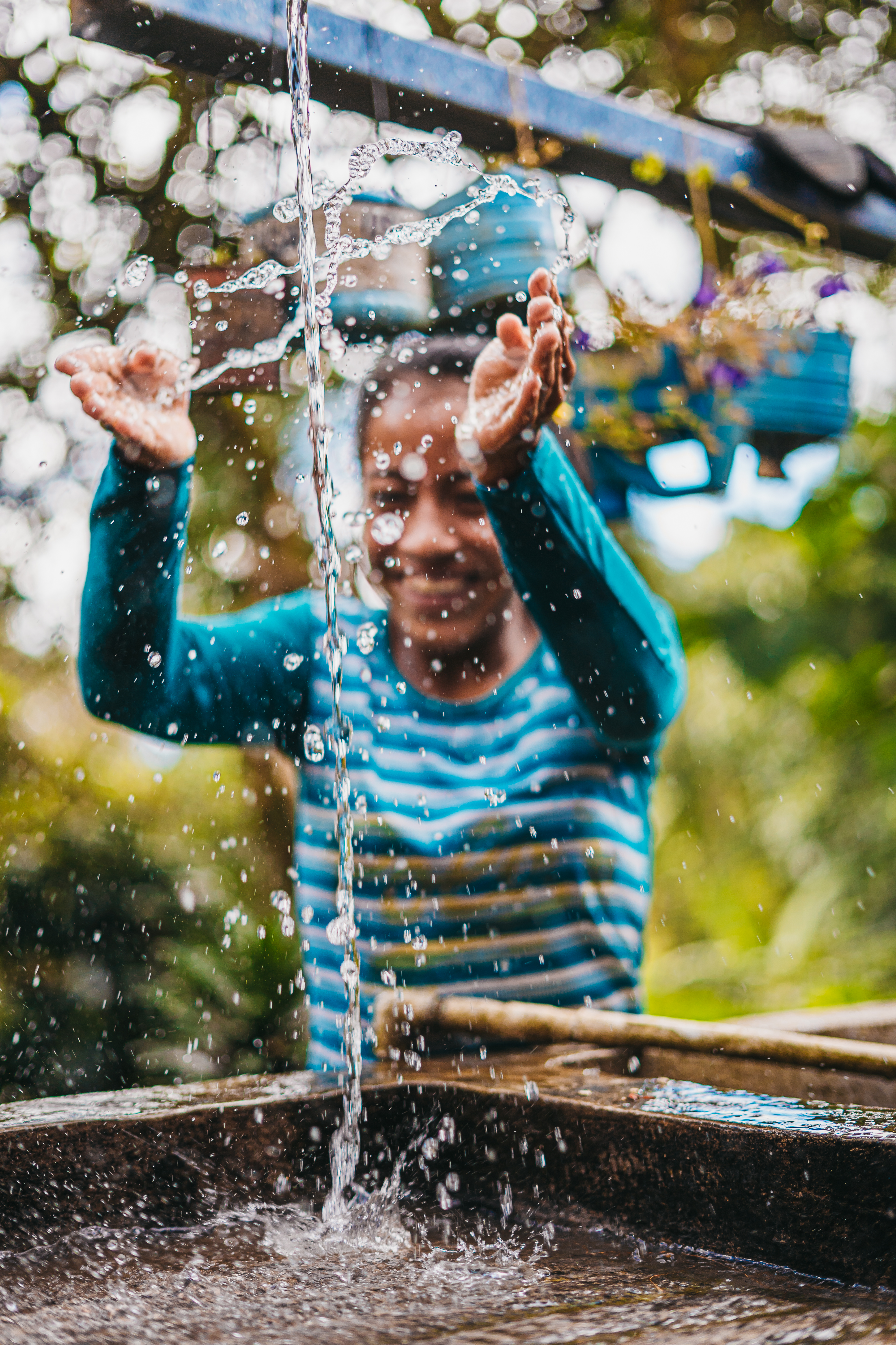 Teenage girl smiling broadly as she plays with the clean water pouring from an outdoor tap at her home.