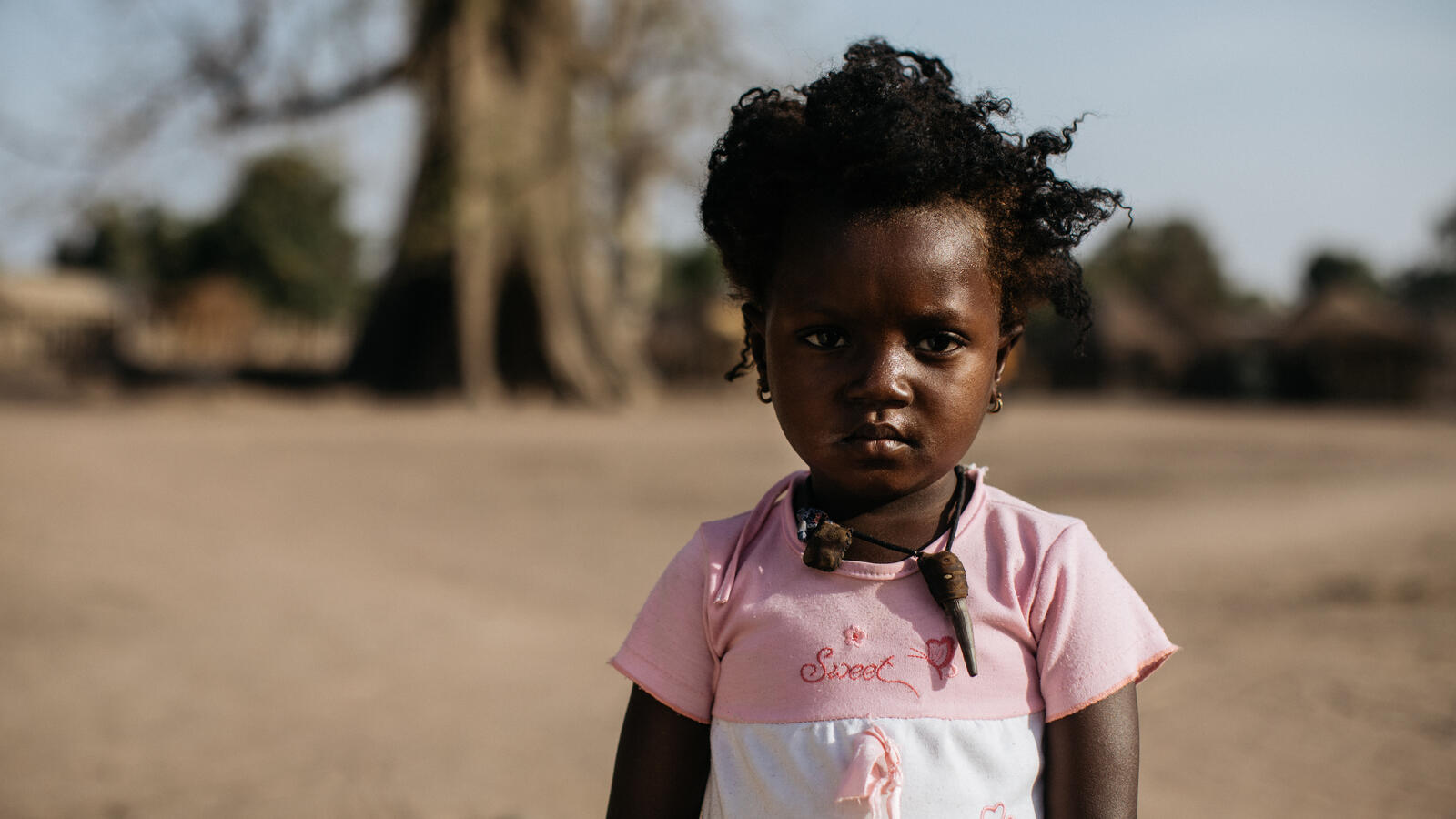 3 year old girl from Senegal smiles to the camera wearing a pink and white top