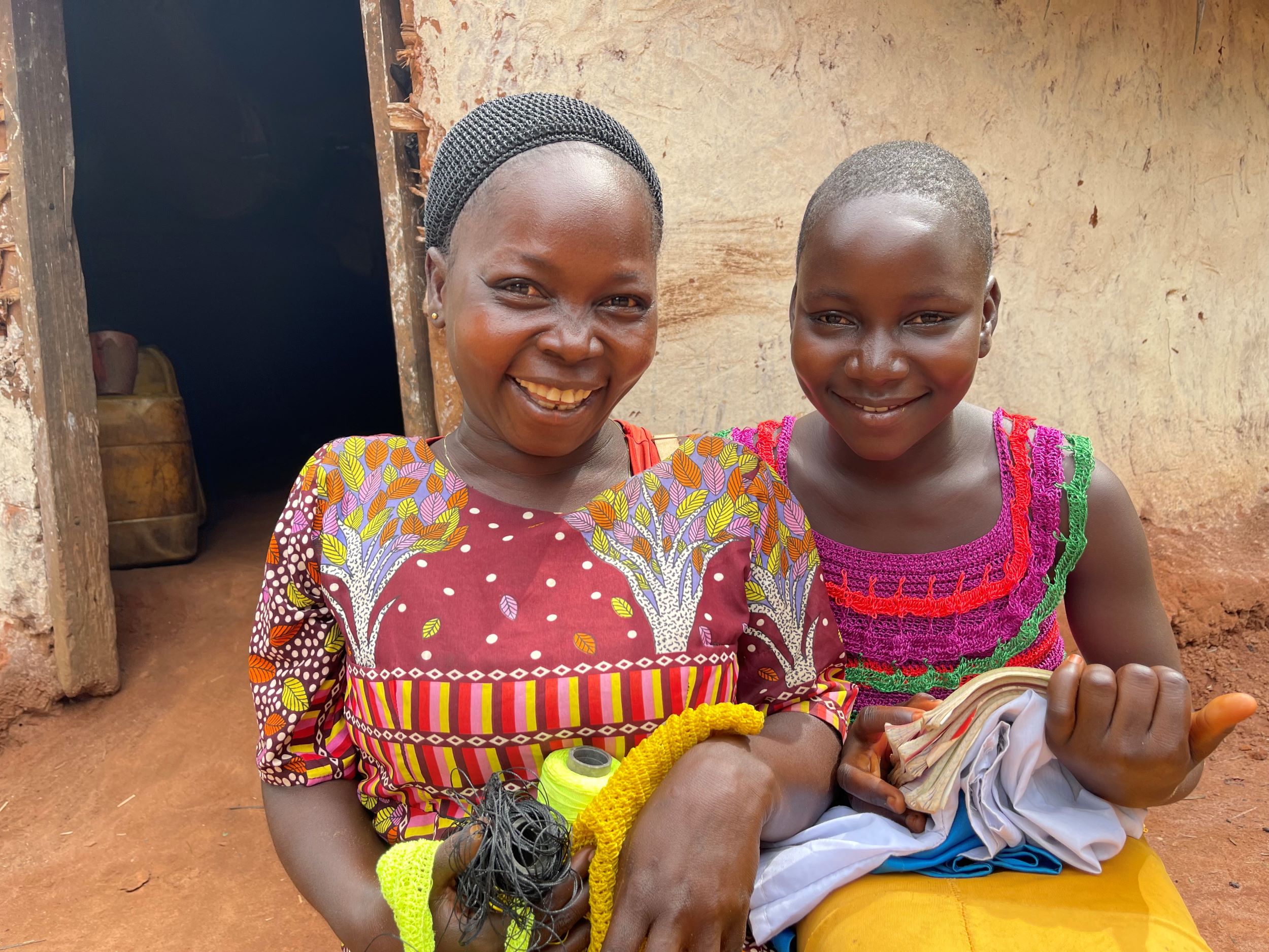 Mother and daughter in colourful clothes smiling in front of their home, DRC 