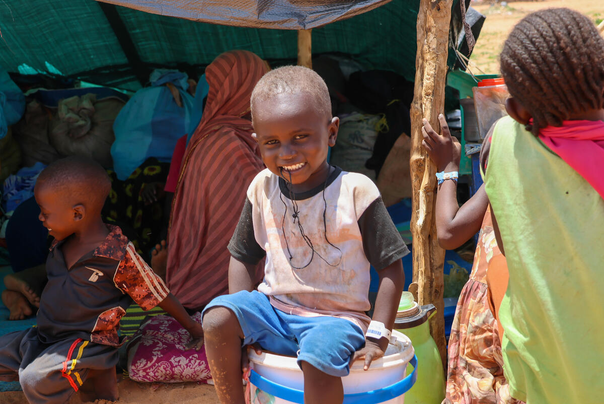 Child stands outside in Chad refugee camp smiles at the camera.
