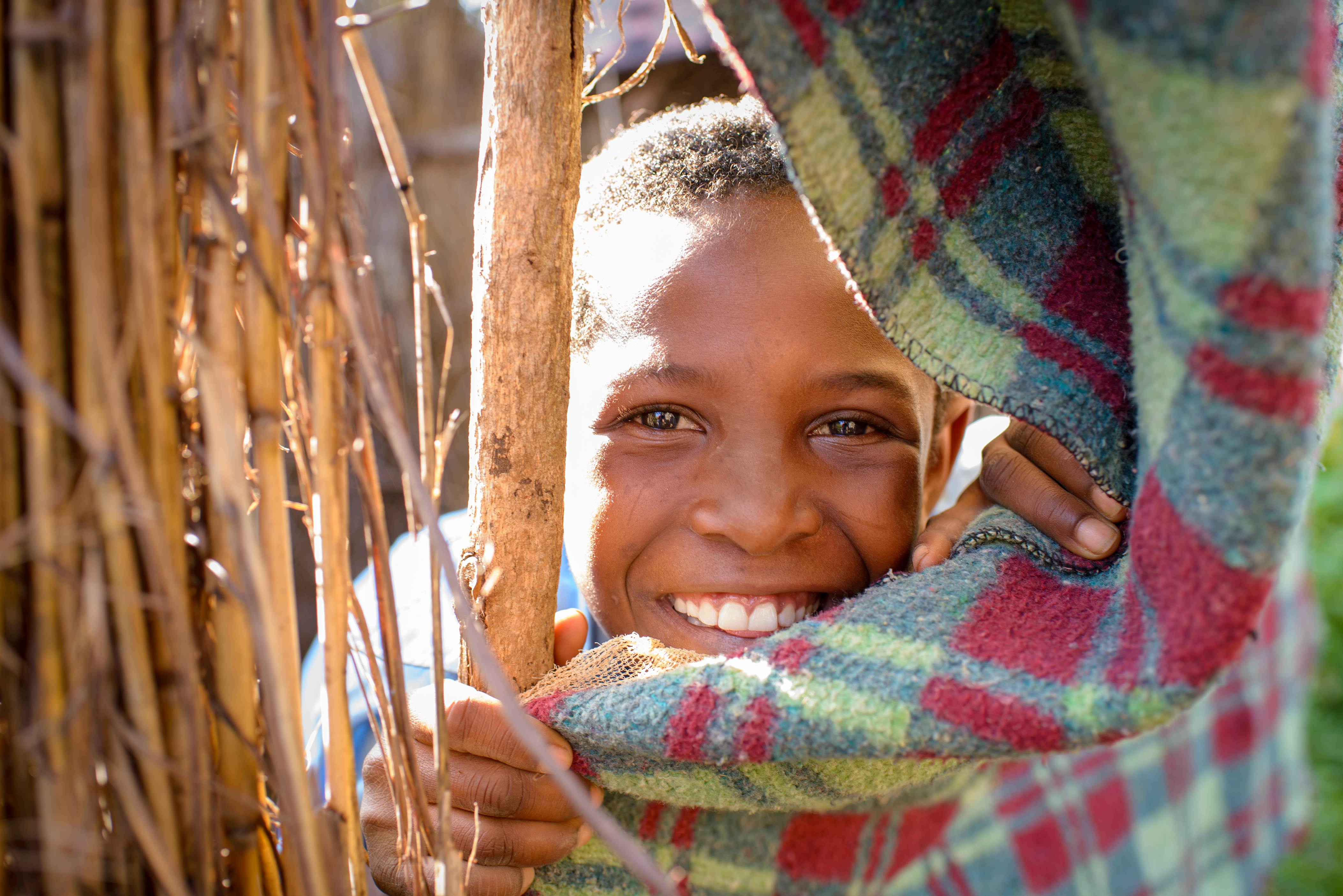 Child from Zambia smiles as they peek through a gap in a curtain
