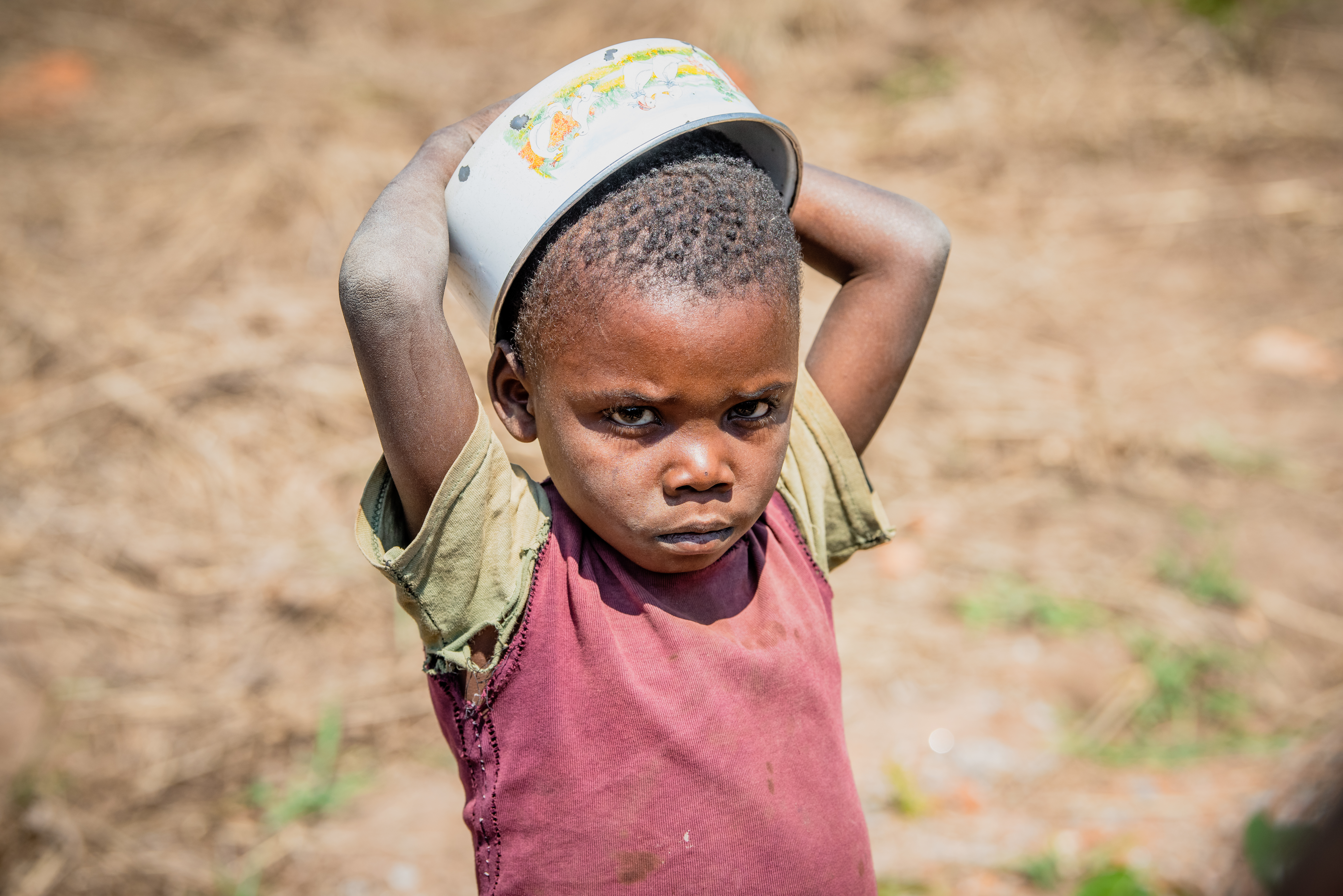 Child in DRC holds an empty bowl over their head in a field