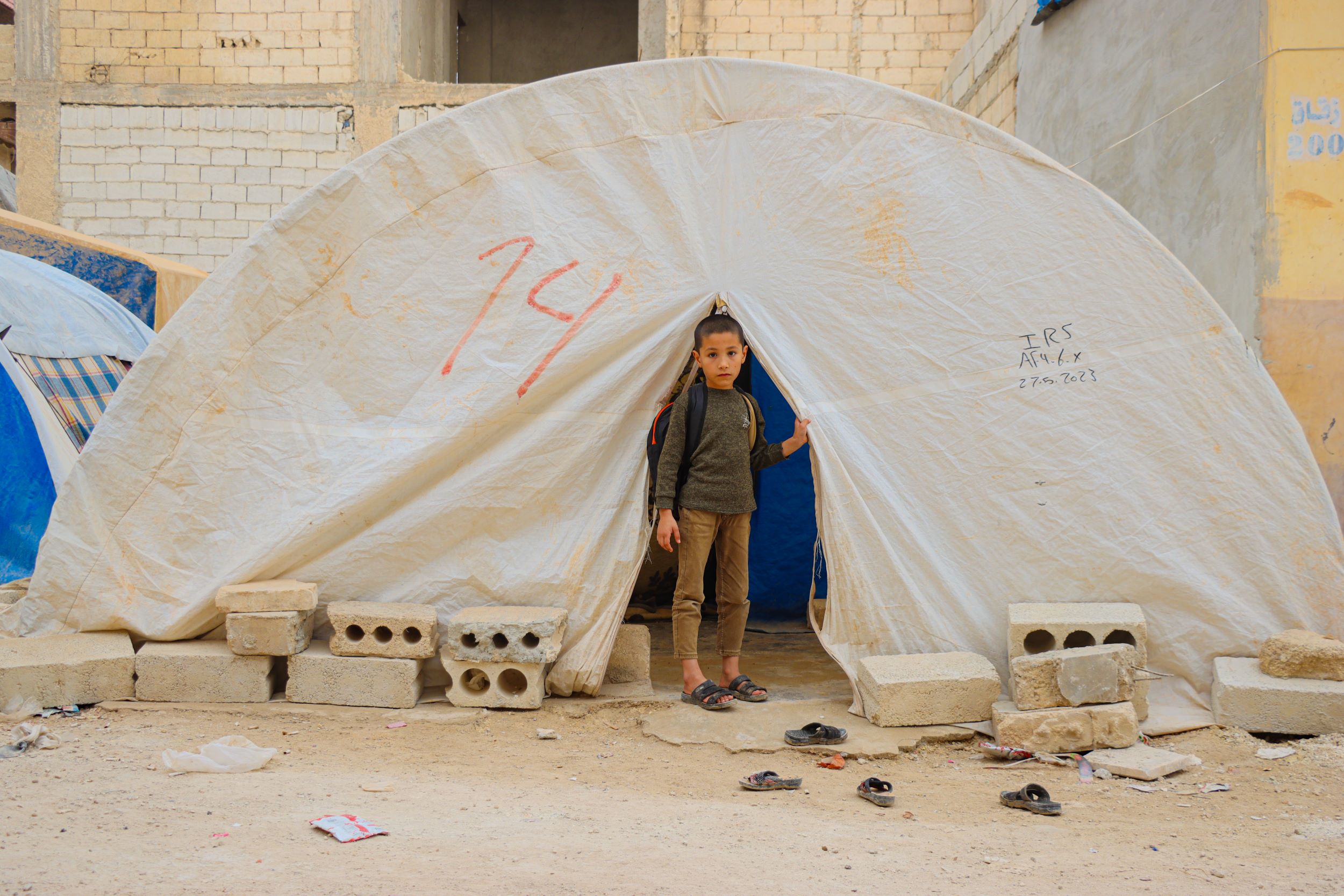 A Syrian boy stands outside his family's tent