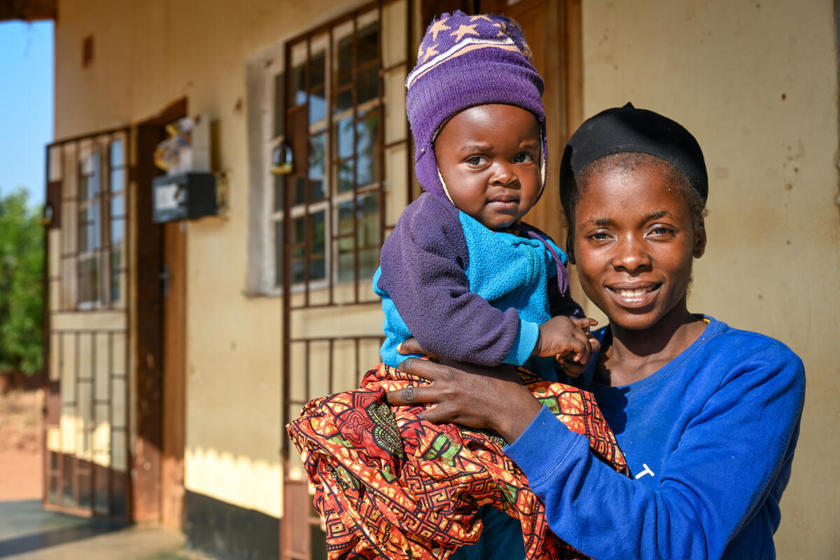 Mother in child in Zambia sit smiling outside of health centre
