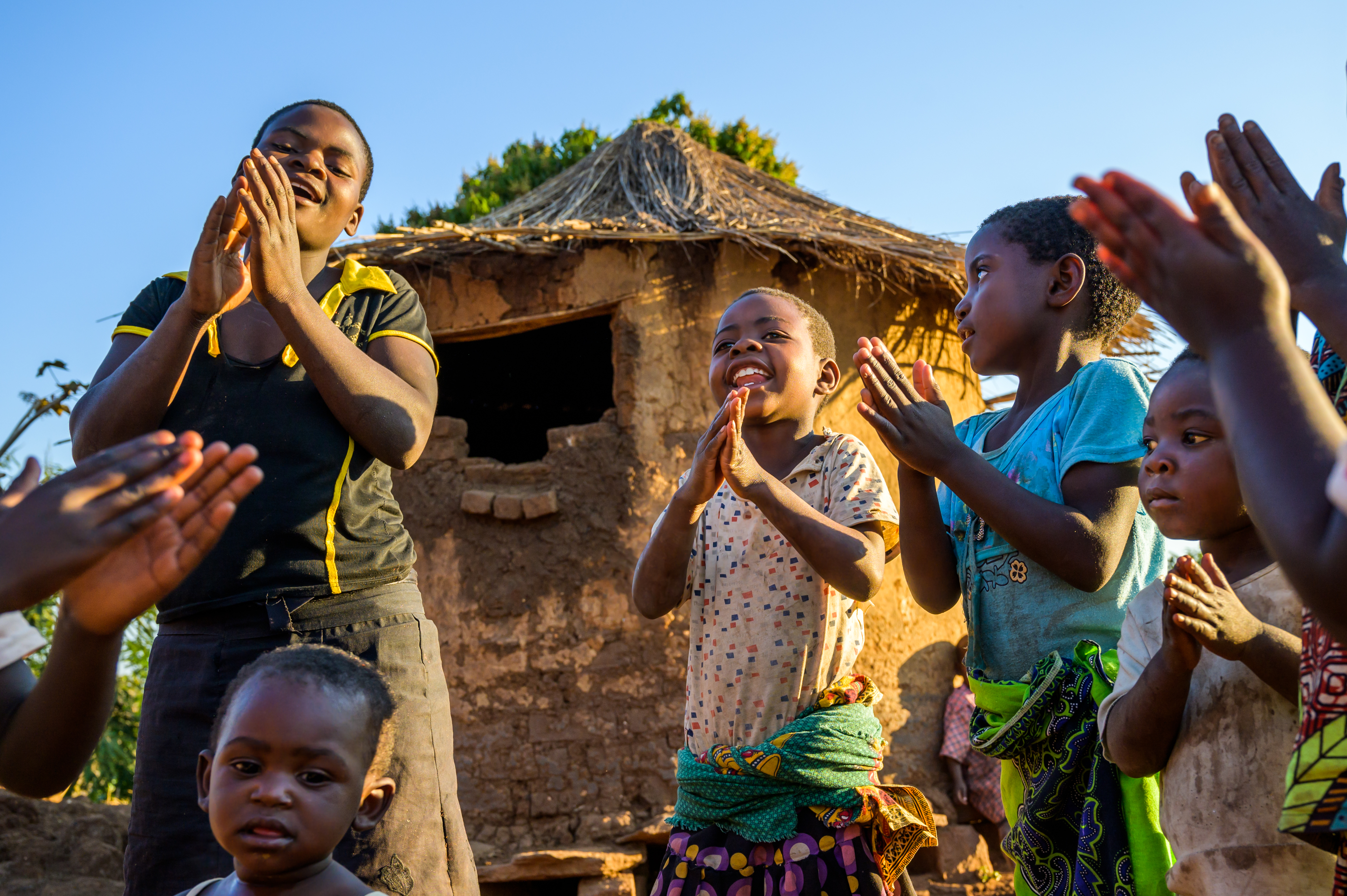 Children dancing and clapping outside their hut in celebration