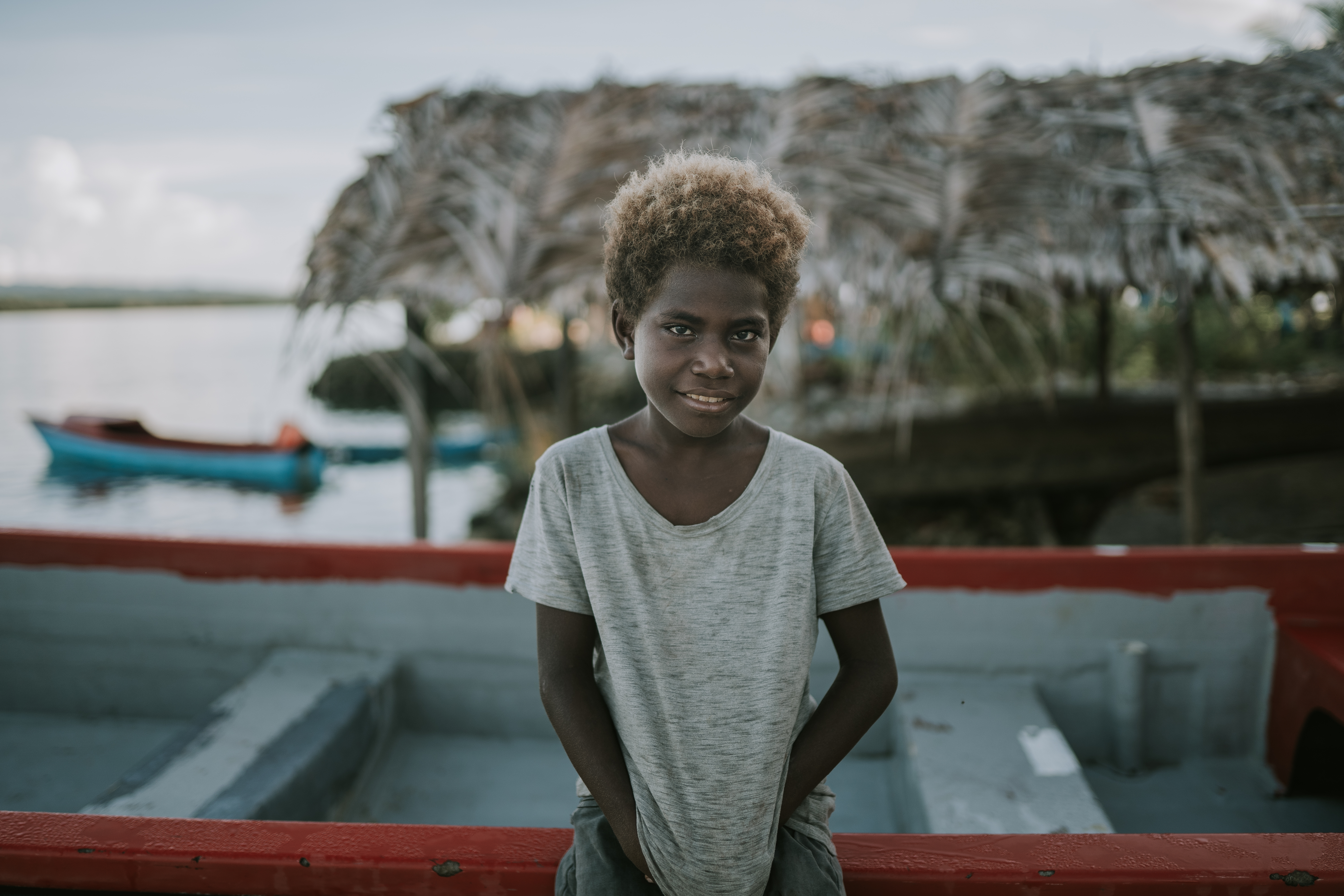 Boy sat on fishing boat on the coast of a small remote south pacific island effected by climate change