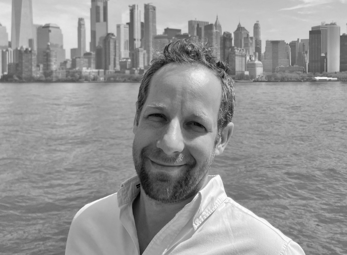 A black and white picture of Alex Harris smiling whilst snapping a selfie