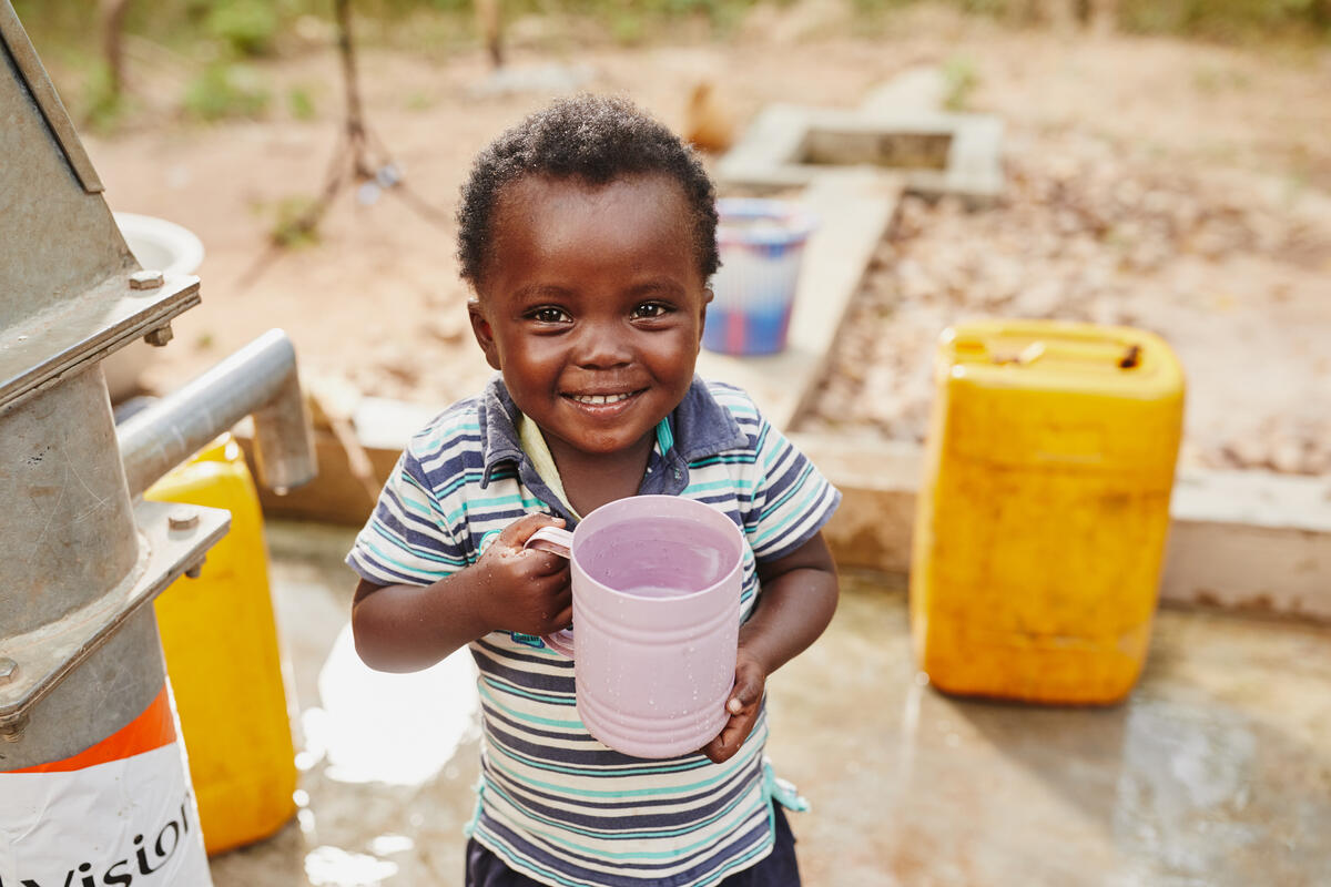 A young boy in Ghana beams as he holds a new cup of fresh, clean water straight from the new water pump