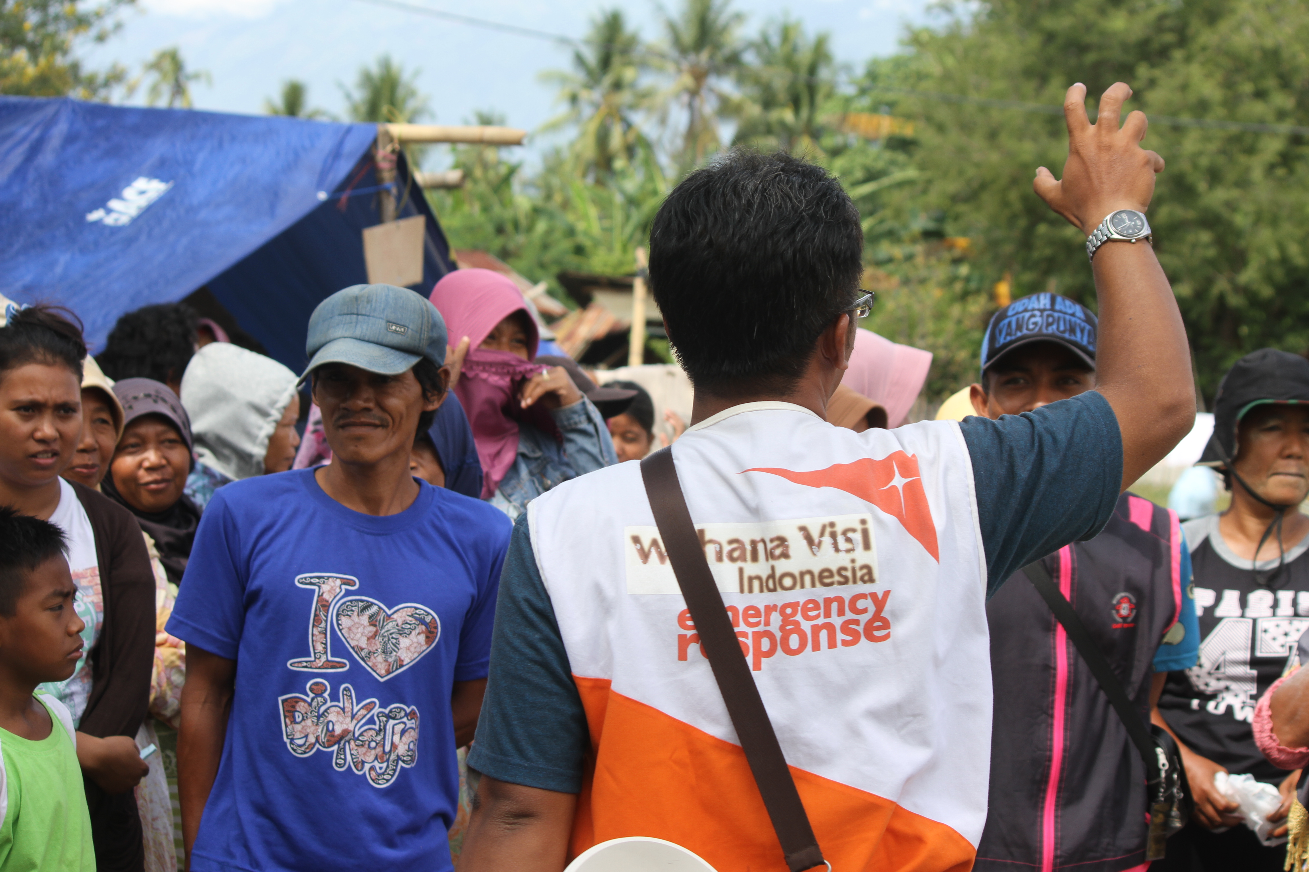 World Vision staff member waves with his back to camera in front of a crowd of people