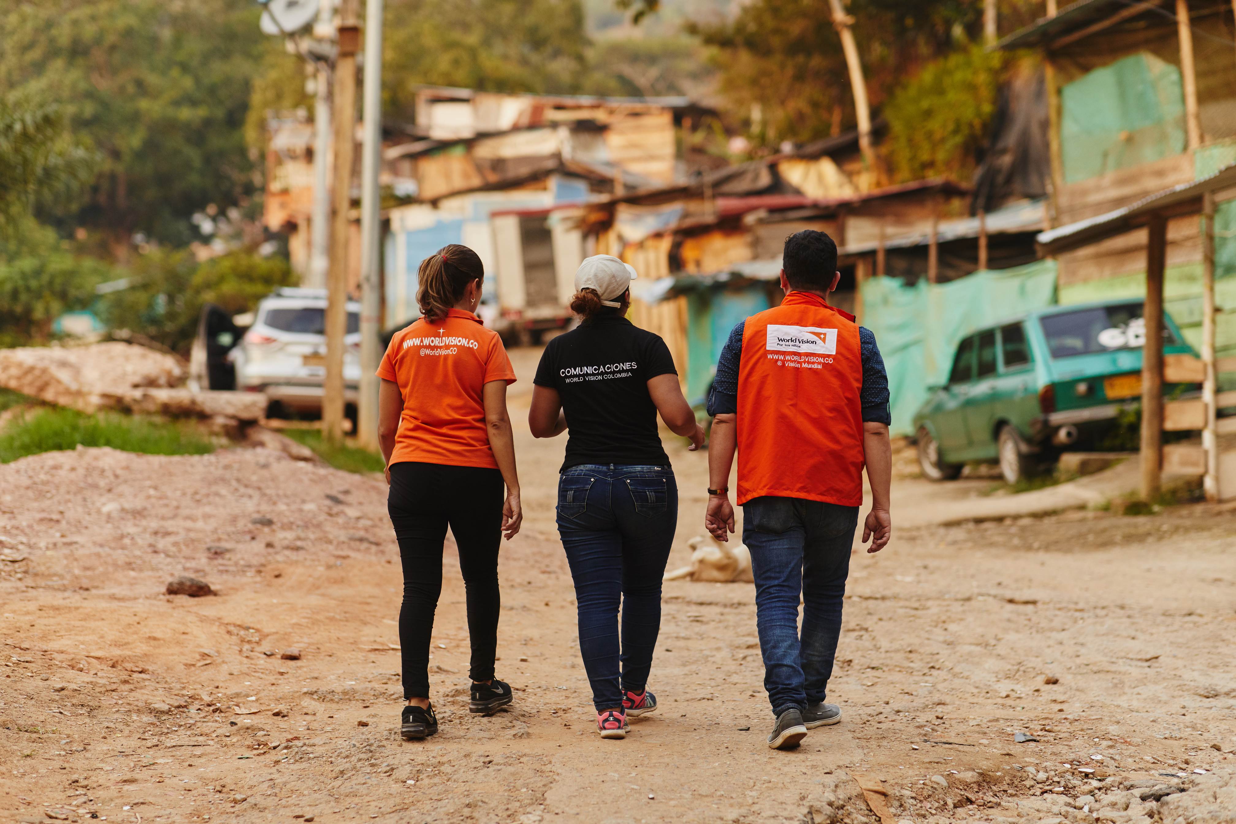 Two World Vision staff walk with a lady, backs to the camera, through streets in Columbia