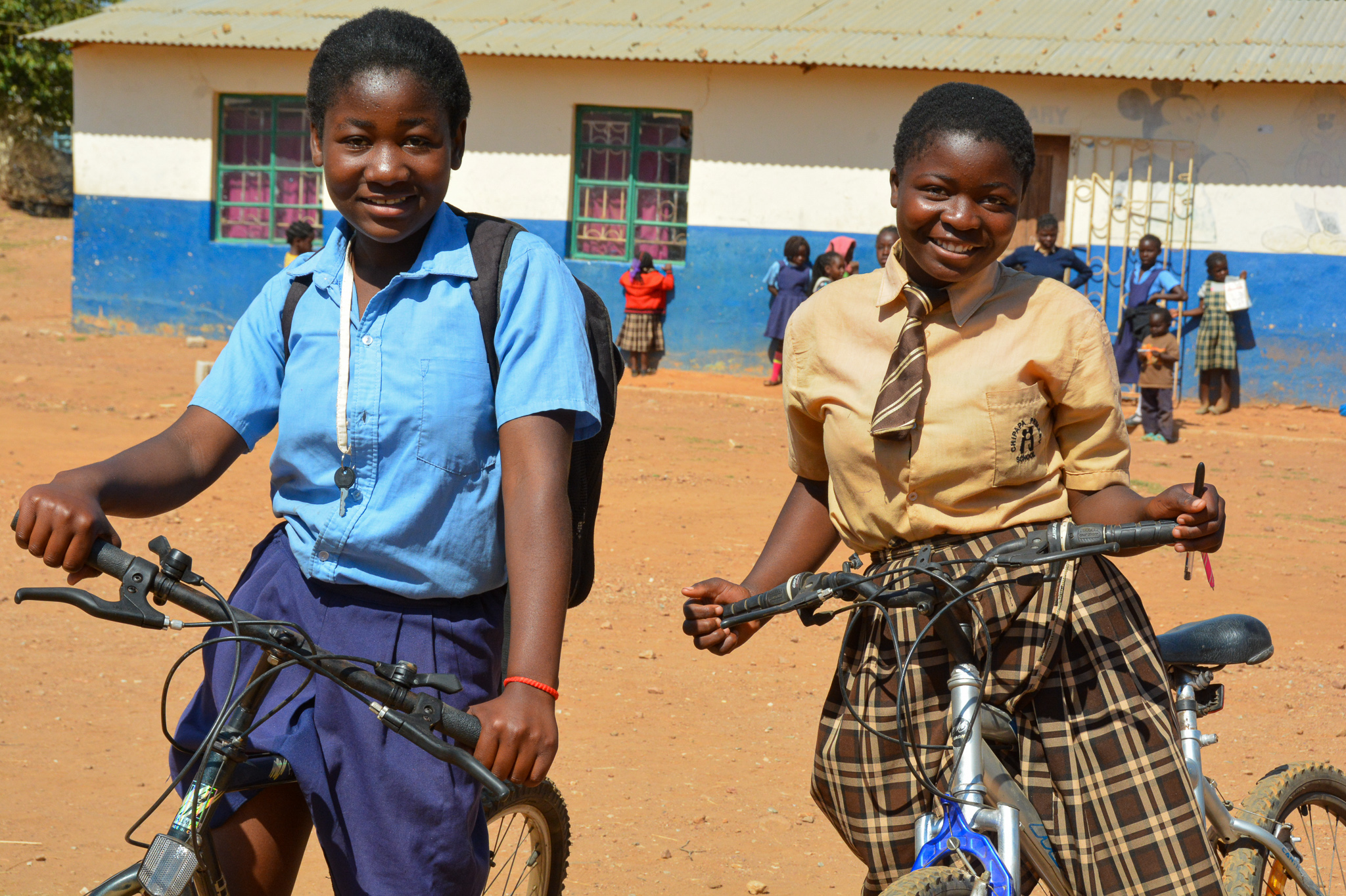 Two girls in their village in Zambia, riding their bikes to school safely.