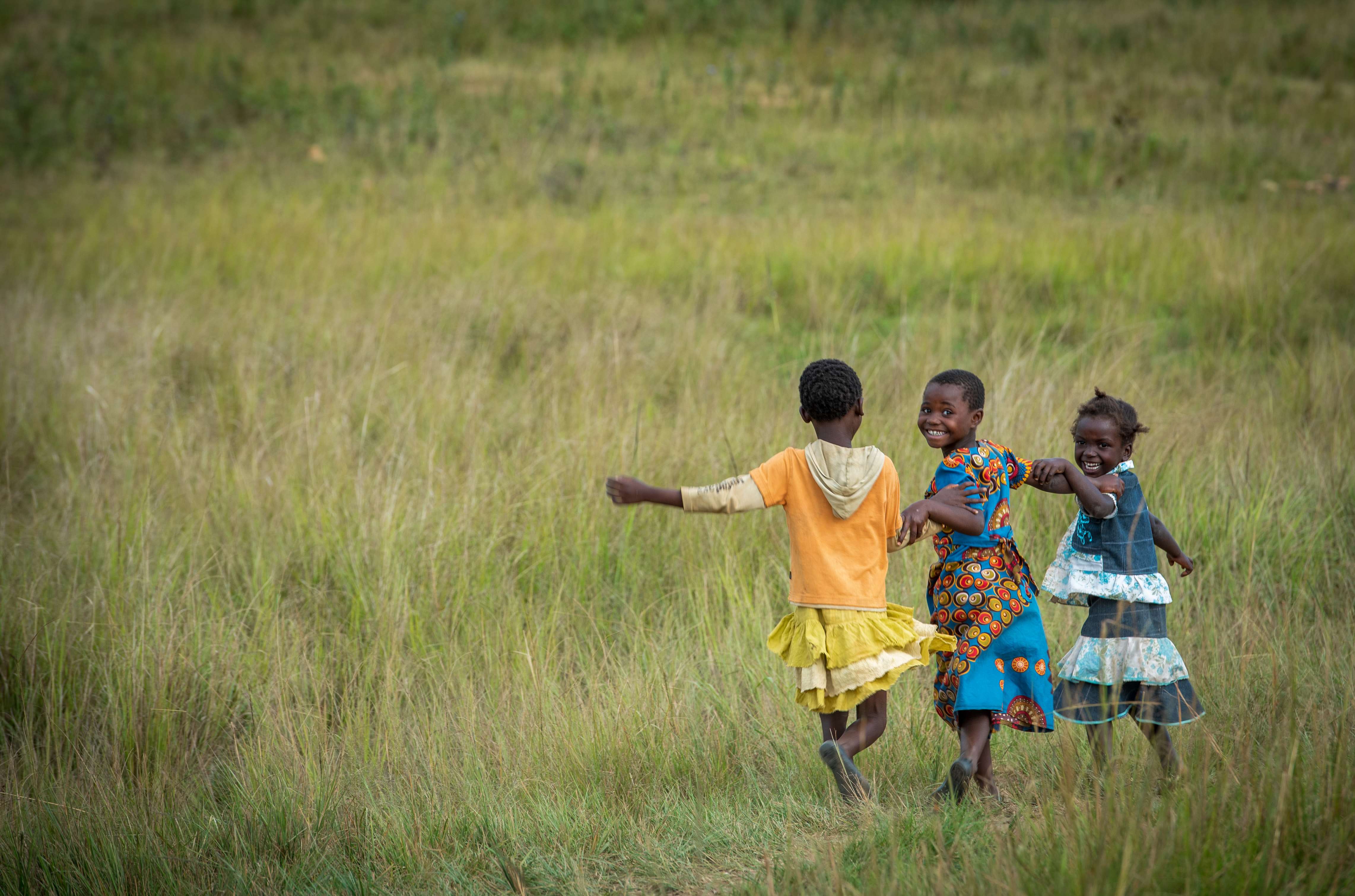 Three children run happily through a field in Zambia