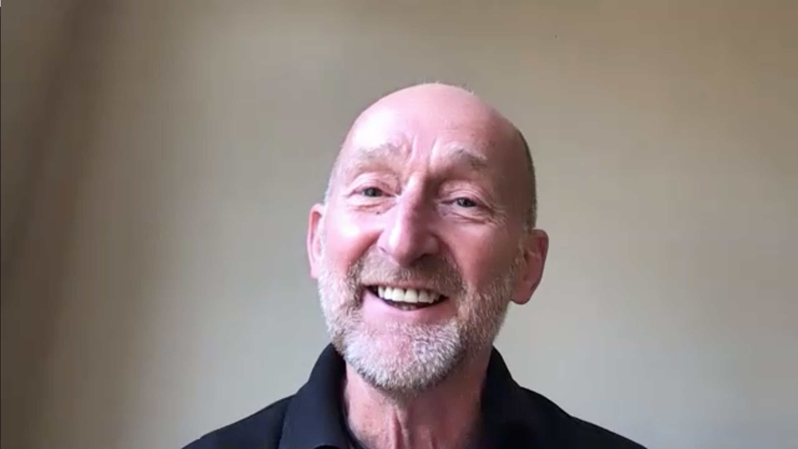 Man in the UK smiles jovially, against a white wall