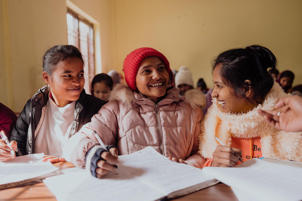 Three teenage girls from Nepal sit at a desk in school discussing their work