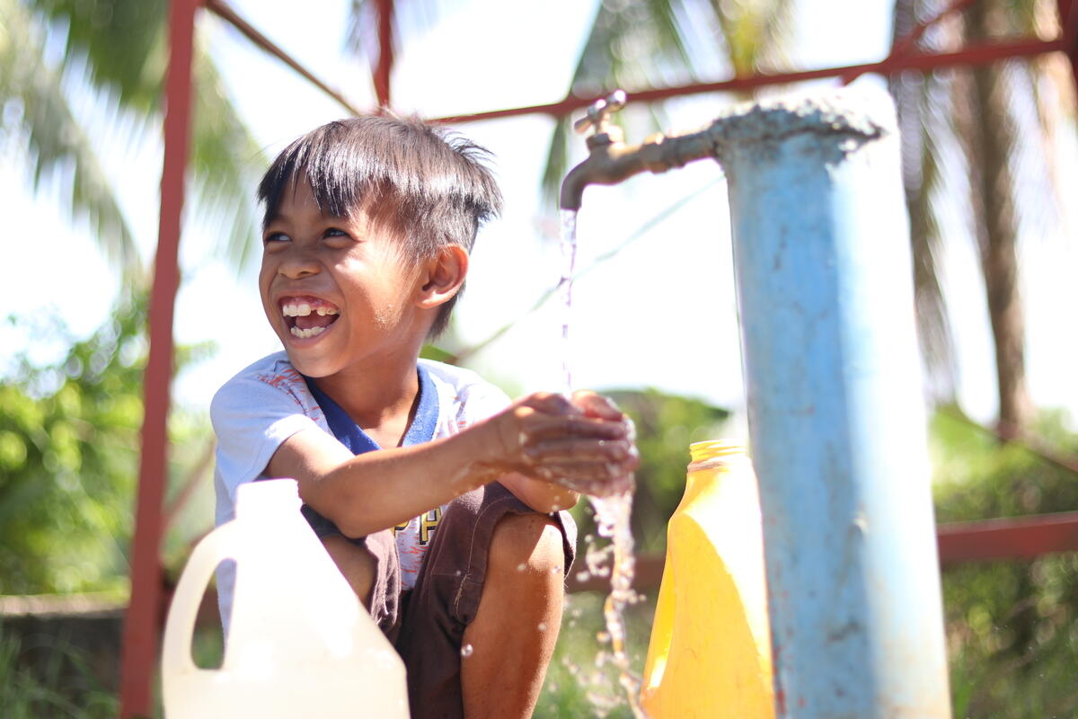 Child in Philippines puts hand under tap and splashes water