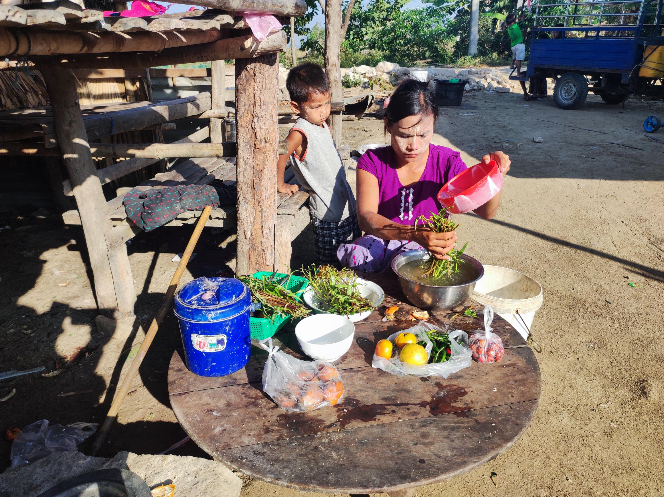 Mother from Myanmar sat on the floor cooking, while her young son looks on