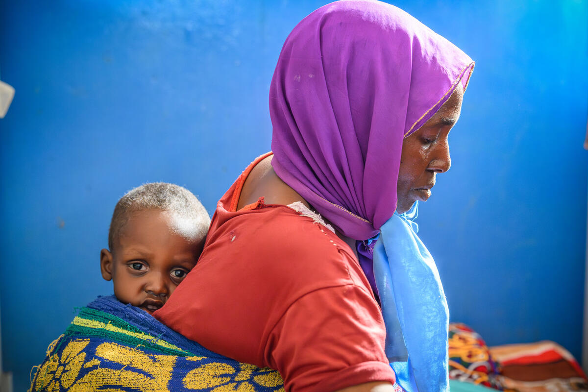 A mother from Sudan carries a baby in a sling on a back
