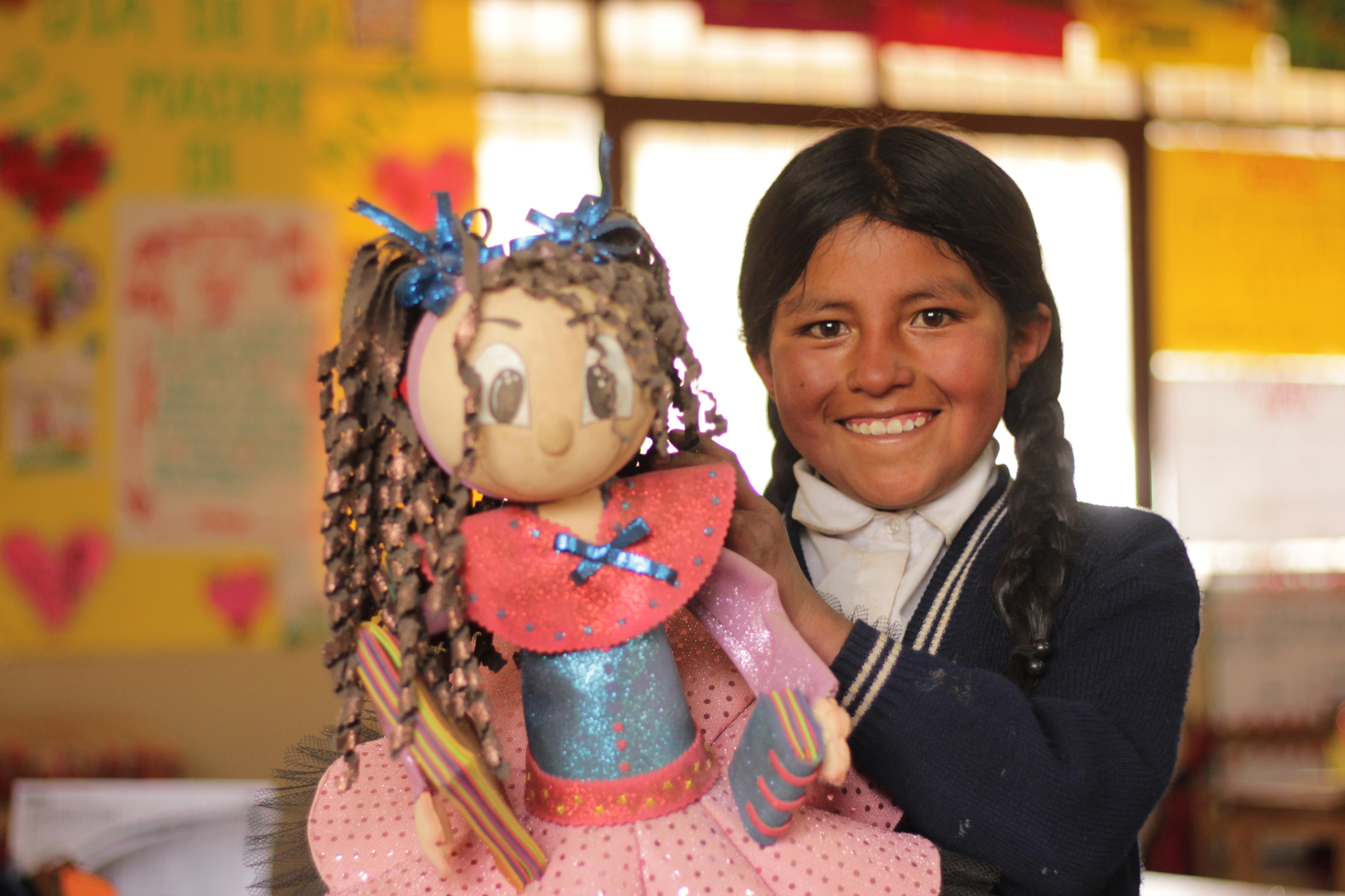 Girl in Bolivia holds up the doll she got in her classroom to help with her education