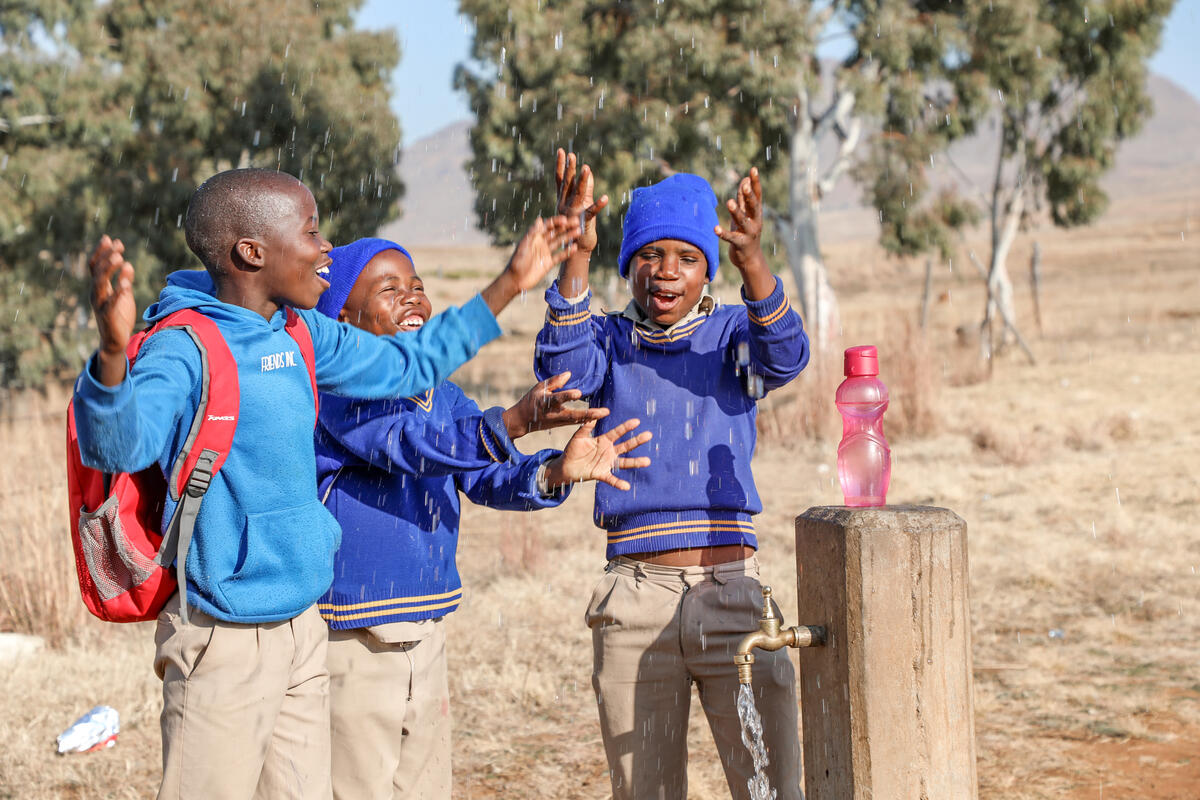 Three boys in their blue school uniform by a water station after a day at school in Lesotho