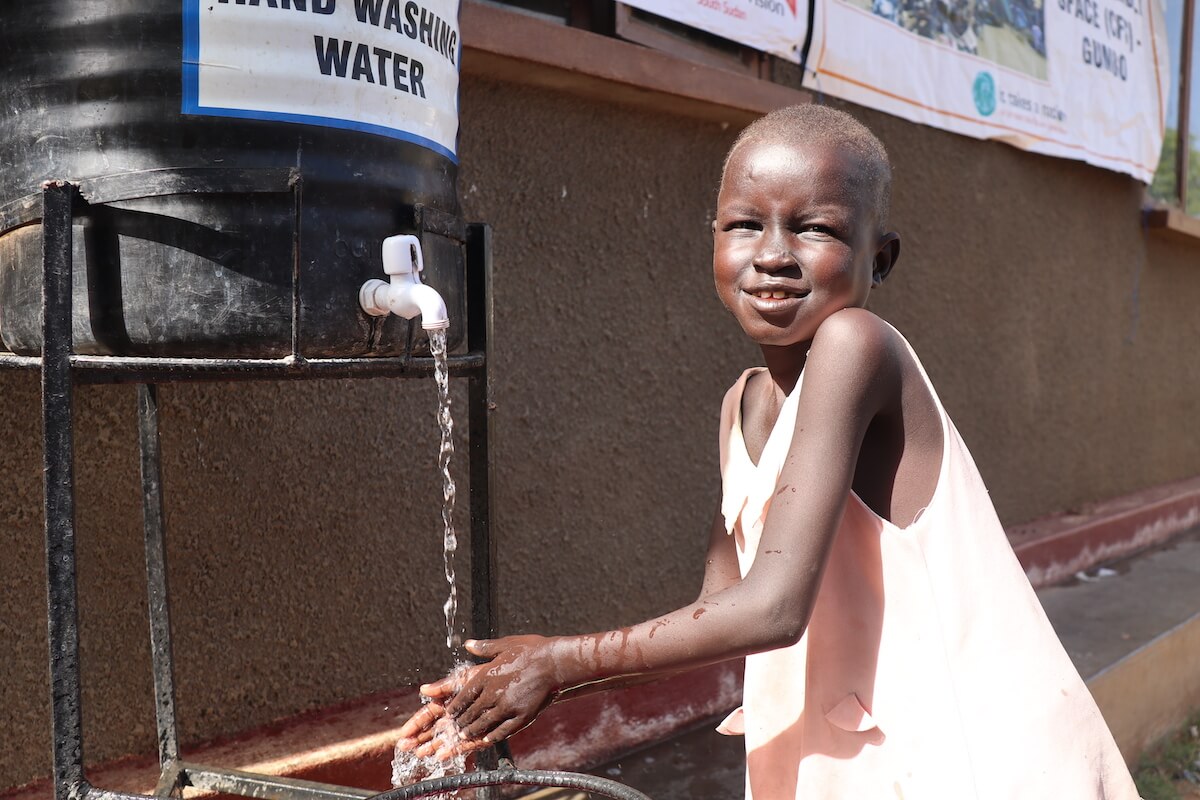 A girl washing her hands under a water pump