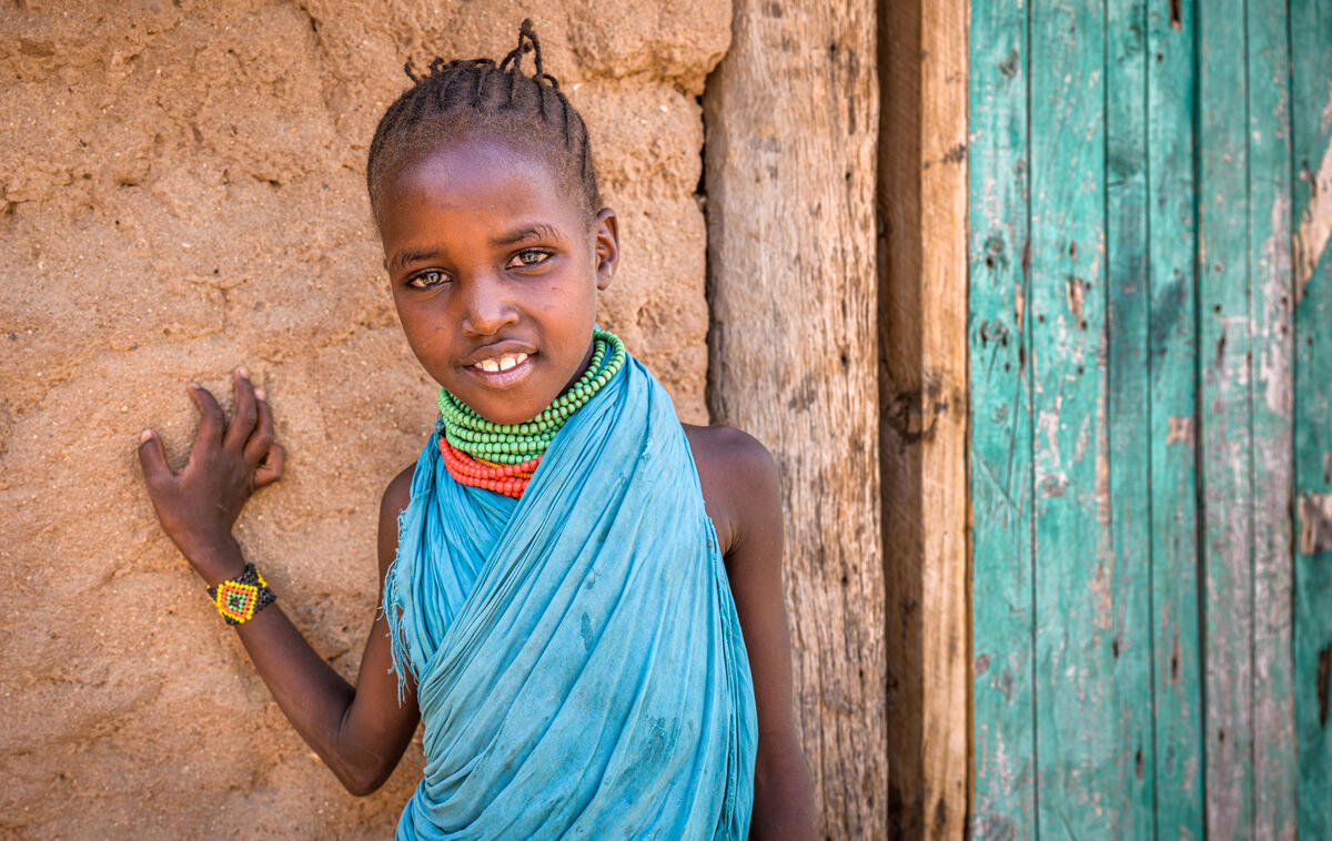 7-year-old Kenyan girl stands outside her home smiling