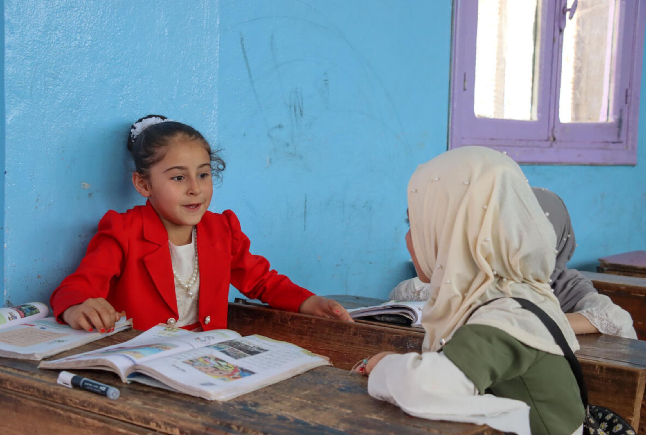 Three children from India smile into the camera, one boy holding a football