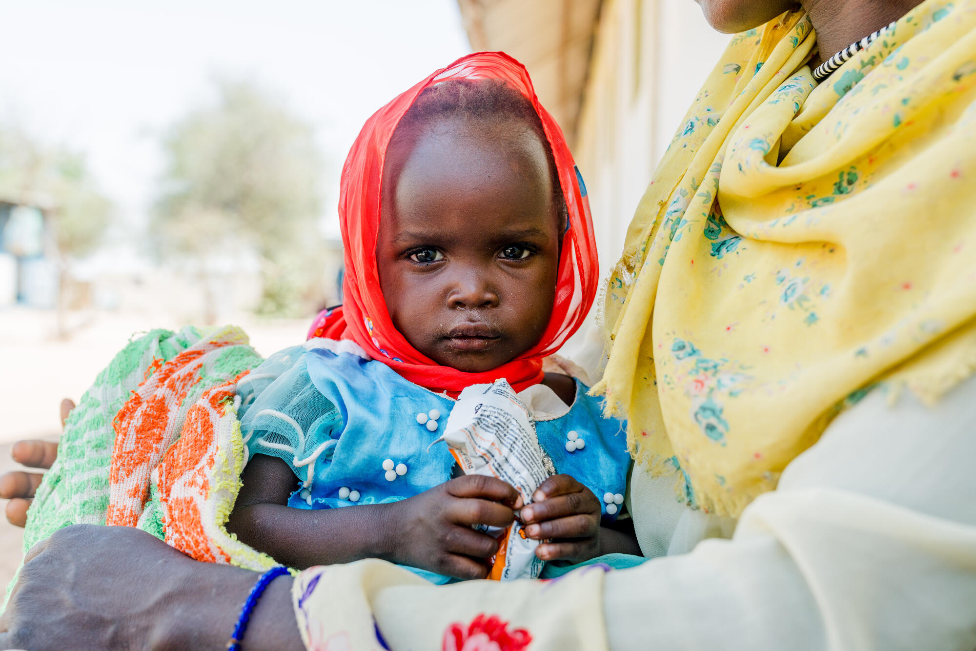 19-month Halima, recovering from malnutrition with the support of World Vision's health clinics in Chad, sits on a lap holding a packet of food.