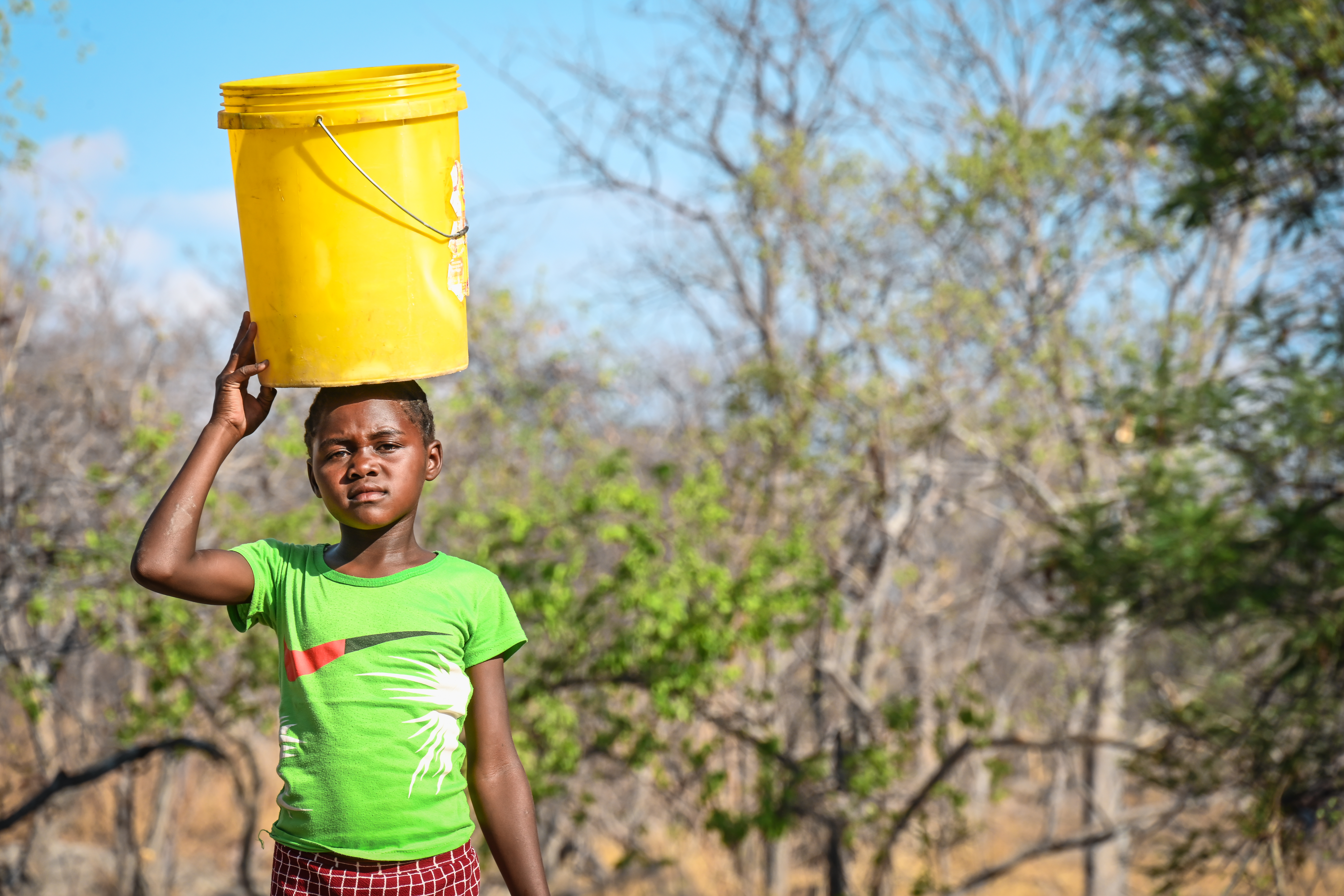 A child in Zambia holds a bucket of water above her head