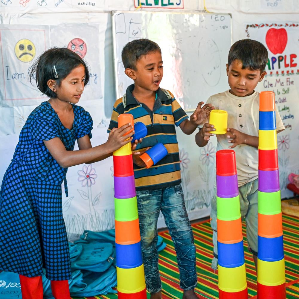 Three children stack colourful cups into towers