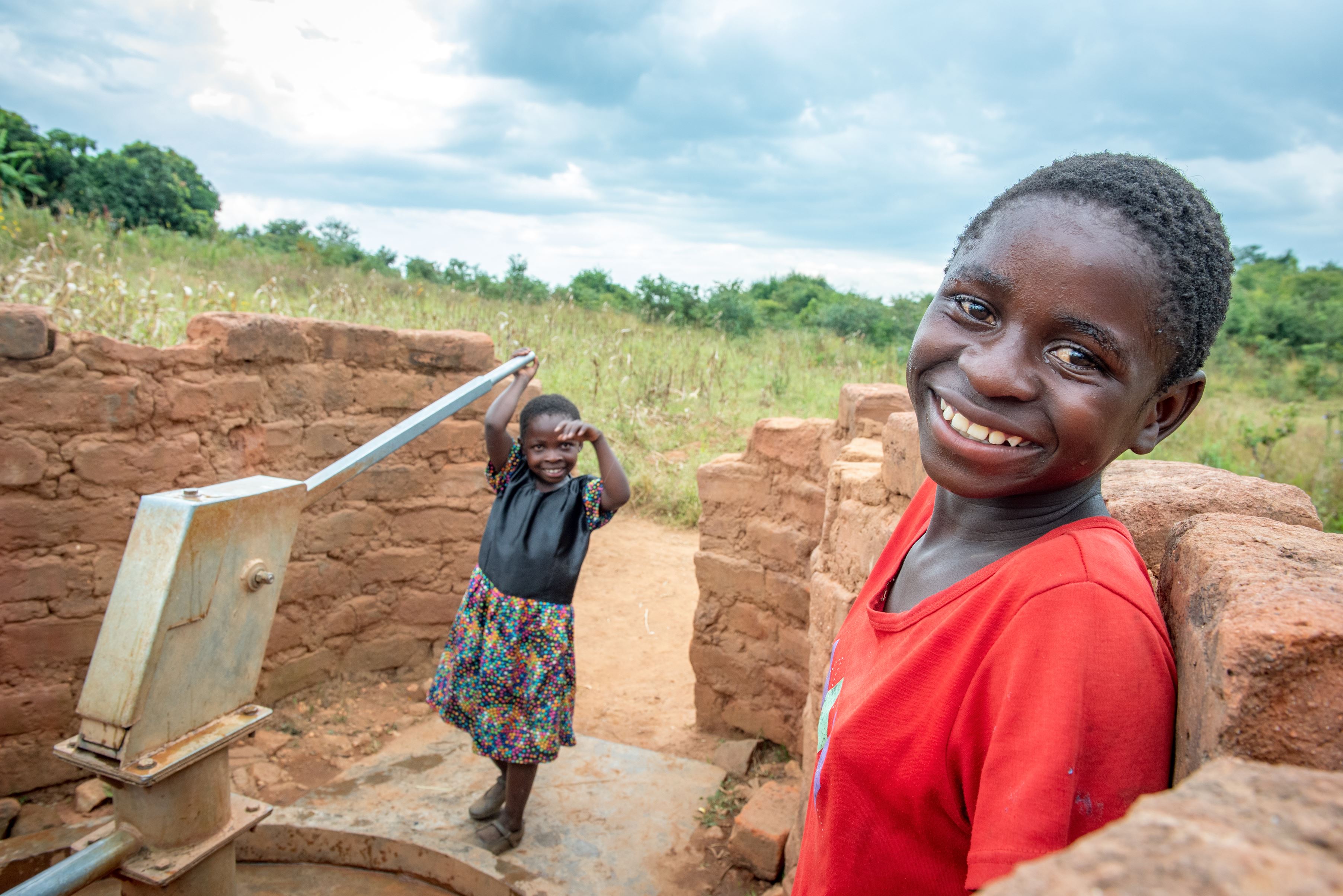 Child smiles next to water pump in Malawi